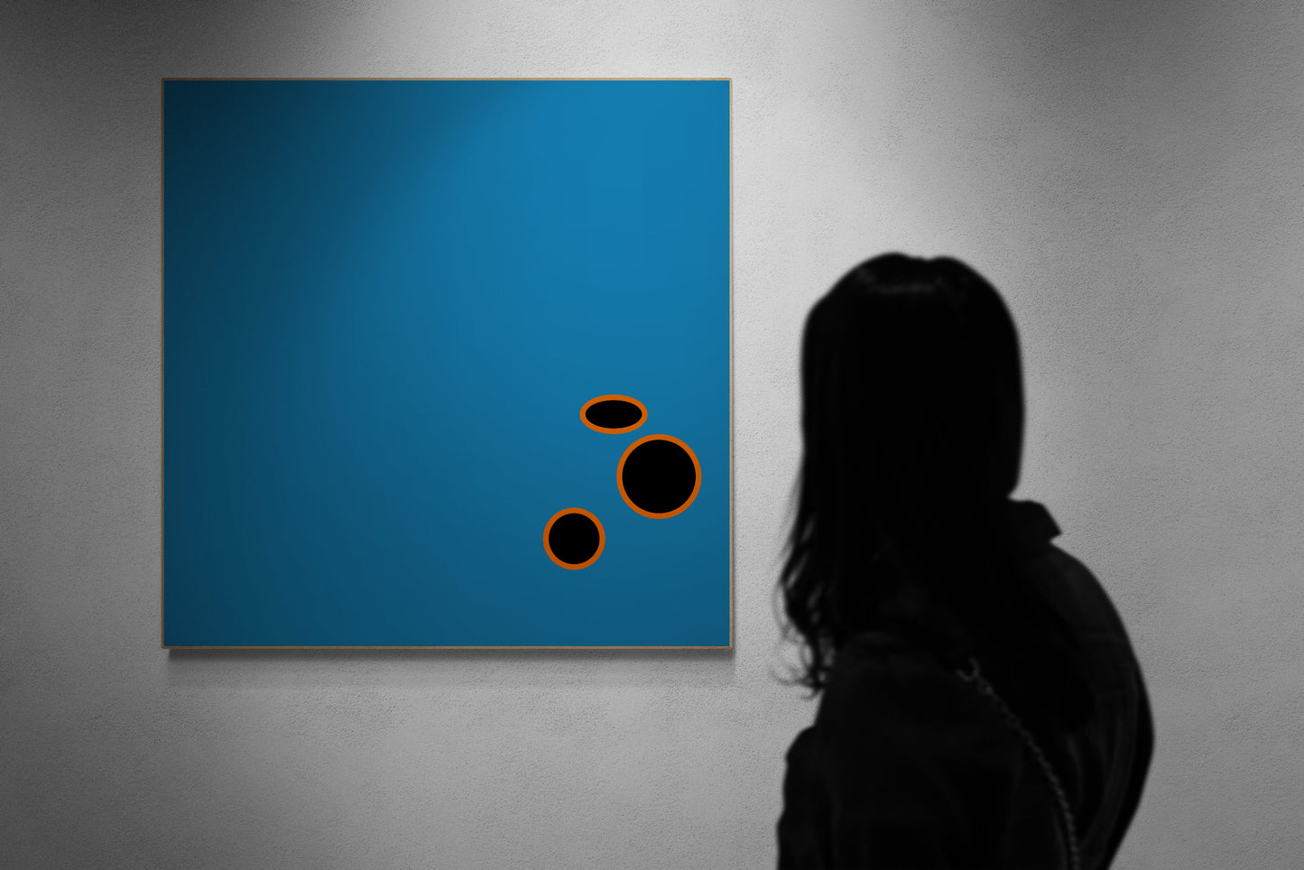 Person viewing abstract art print with blue square and black circles on a gray wall