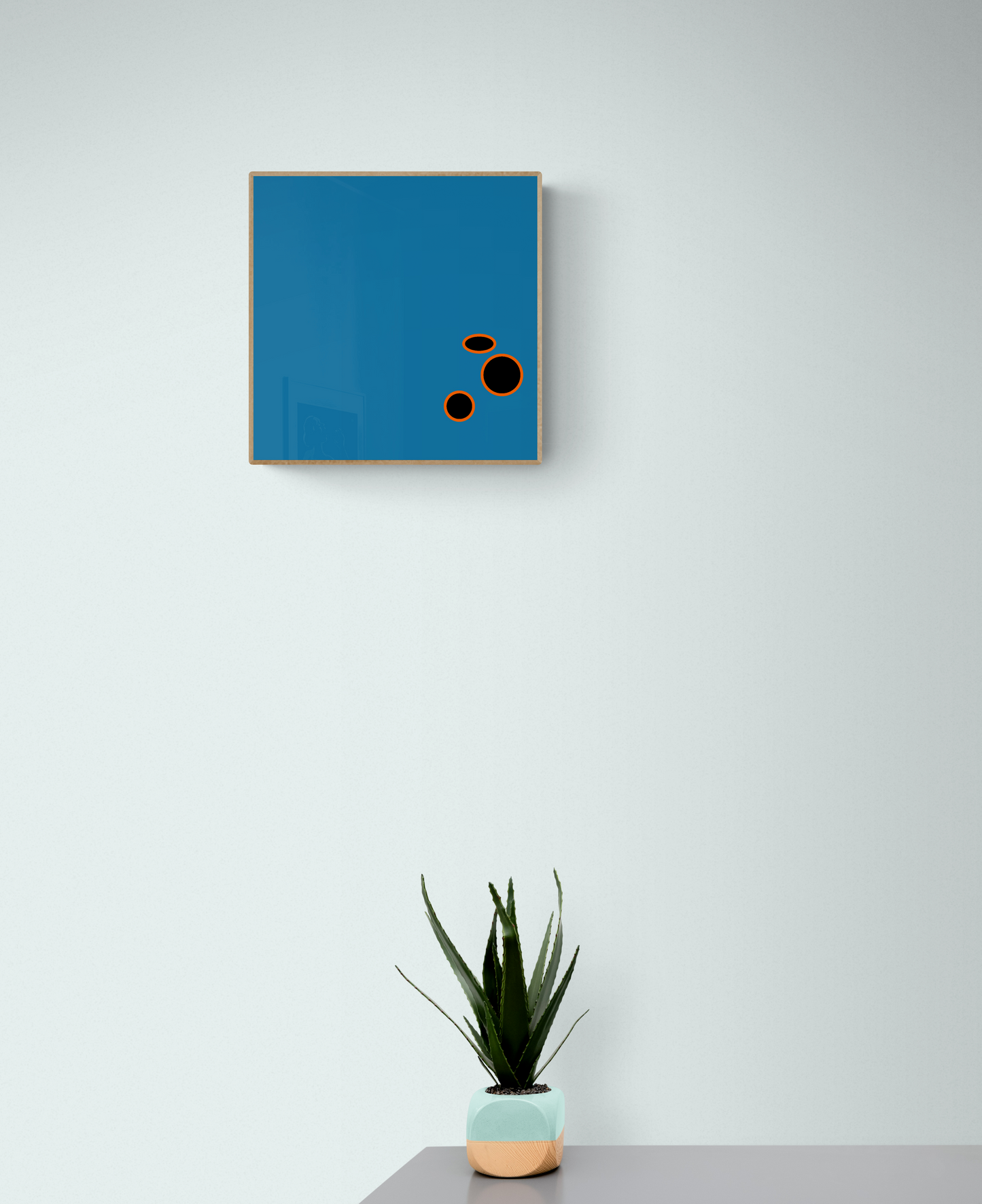 Blue abstract art print with black circles on a light grey wall, accompanied by a potted plant.