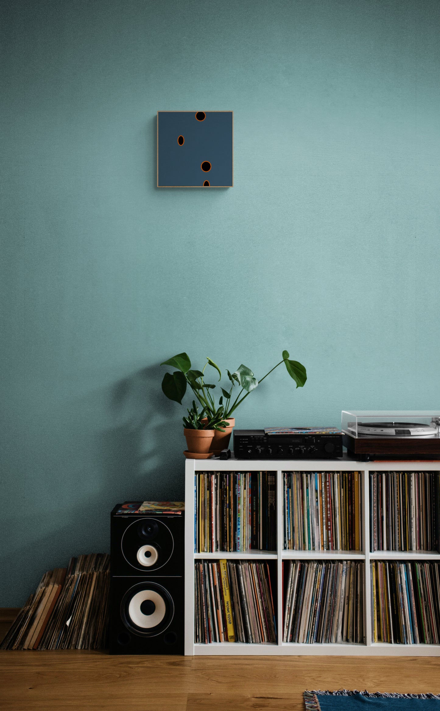 Record player and collection on a wooden shelf against a teal wall with a plant and grey abstract wall art print