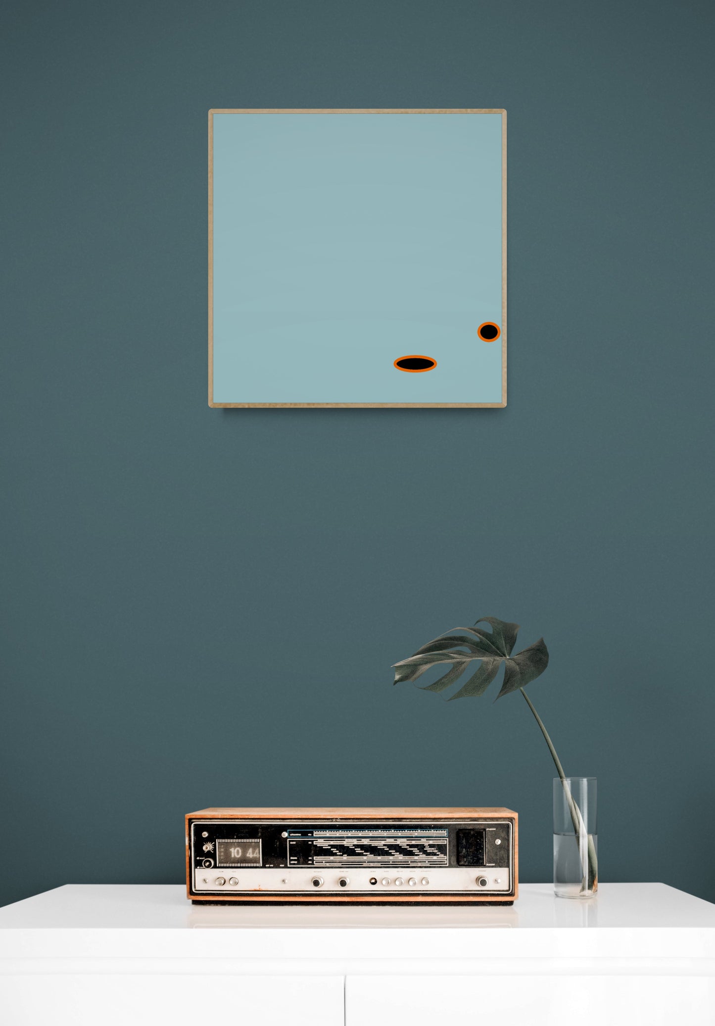 Abstract light blue art print on a teal wall with a vintage radio and plant below.