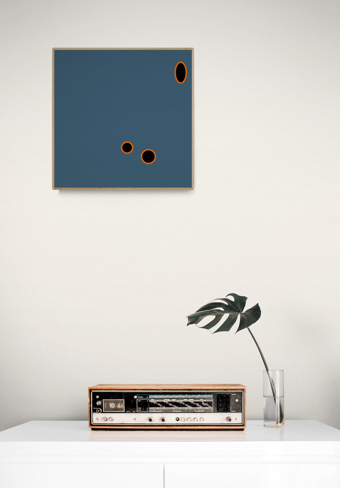 Abstract grey art print on a white wall with a vintage radio and plant below.