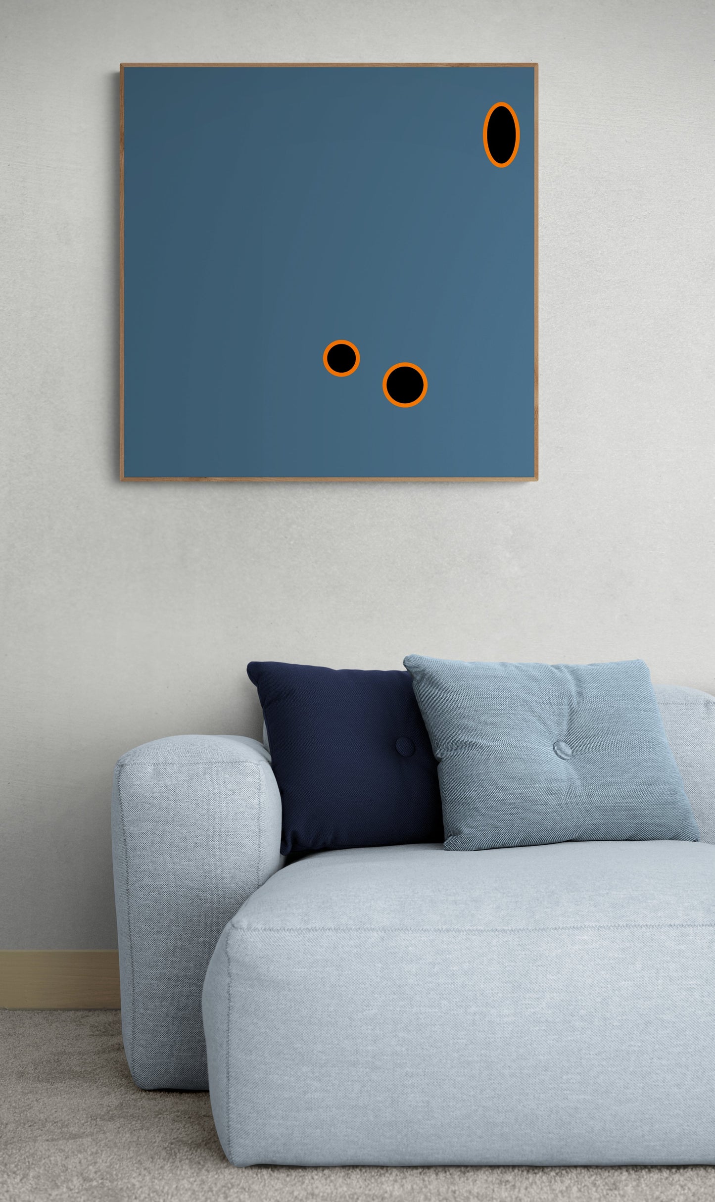 Abstract art print with black circles on a blue background above a gray sofa with cushions.