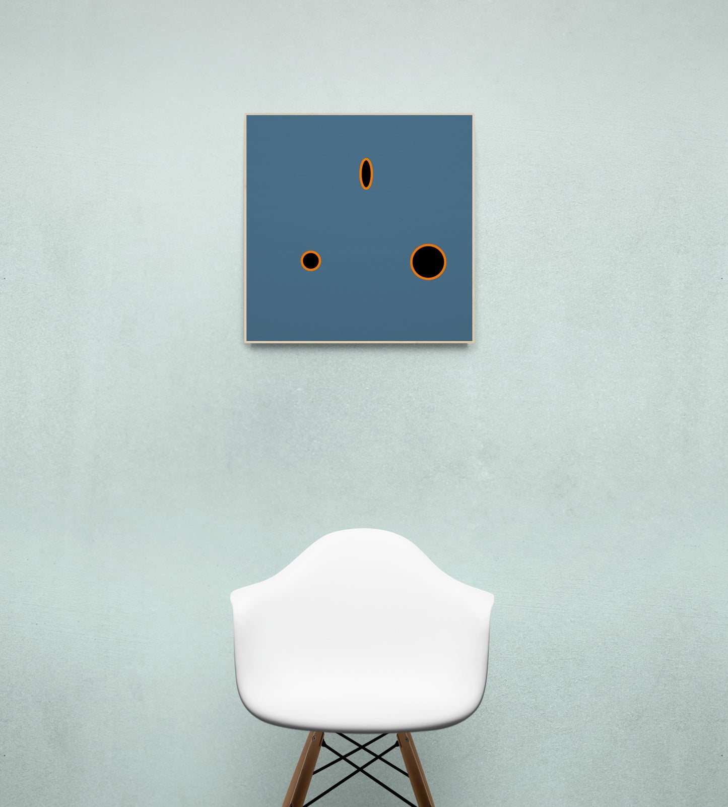 Grey abstract art piece print with black and orange circles on a blue square against a light green wall, with a white chair below.
