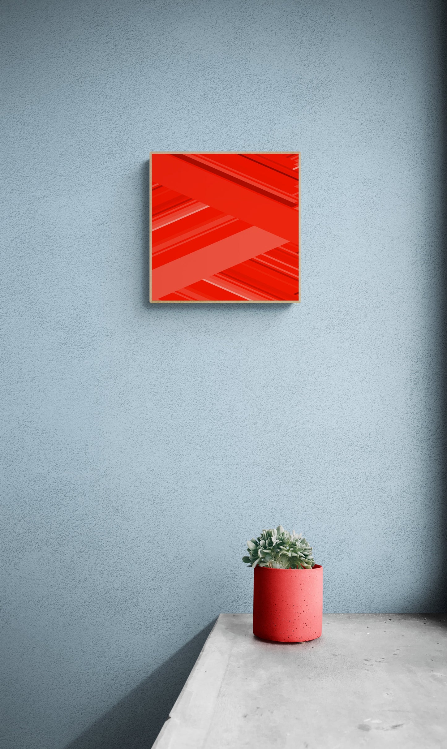 Art print of abstract red design with geometric shapes on a red background on a blue wall with a red planter and plant below.