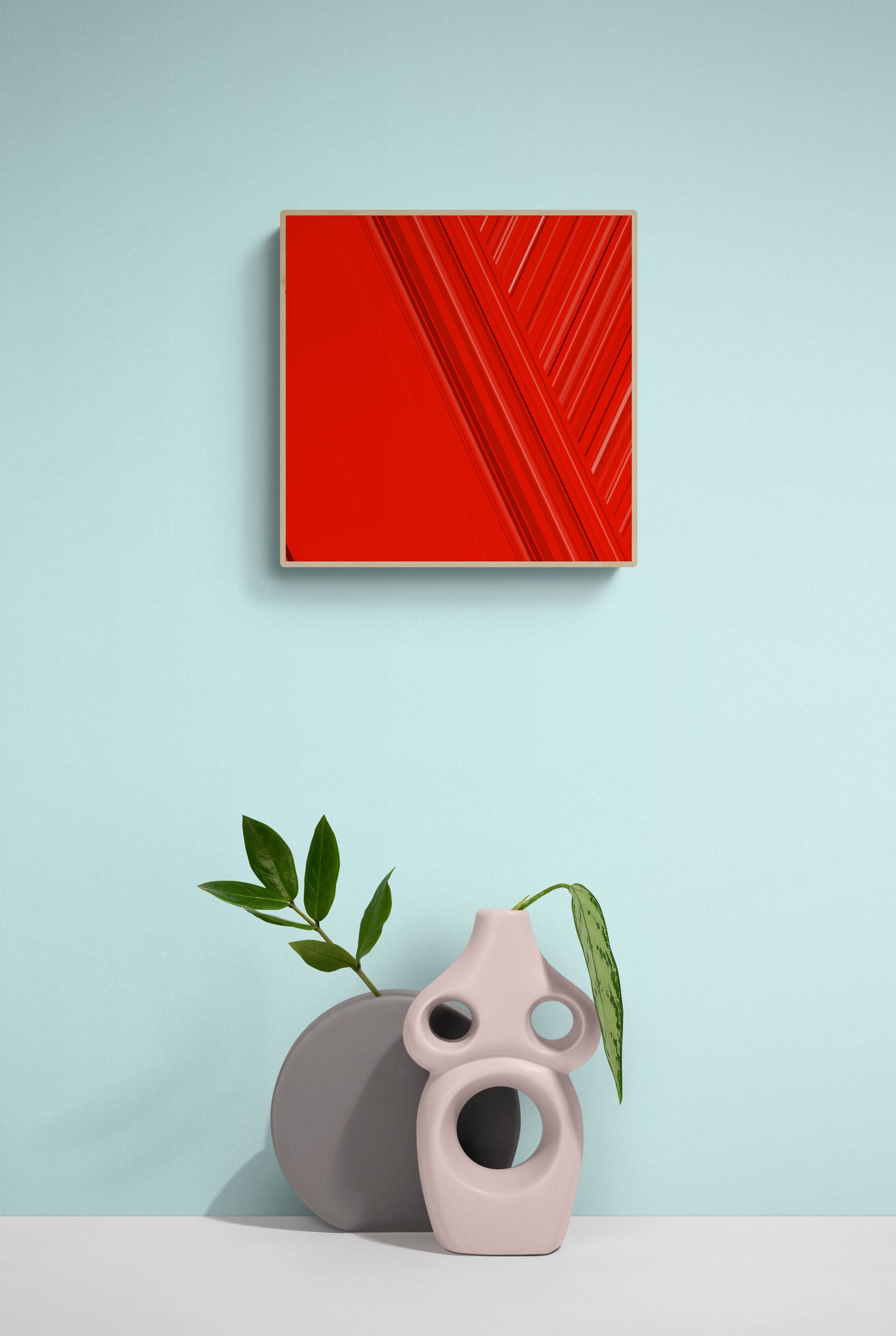 Art print of abstract red design with geometric shapes on a red background on a light blue wall with two decorative vases and a plant.