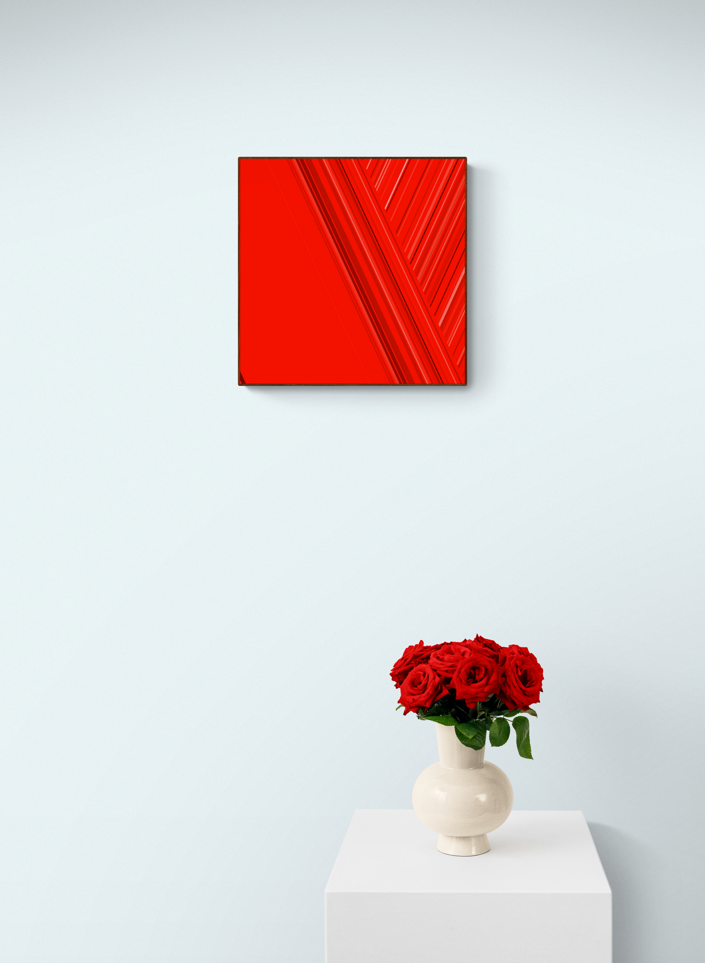 Art print of abstract red design with geometric shapes on a red background on a white wall with a vase of red roses below.