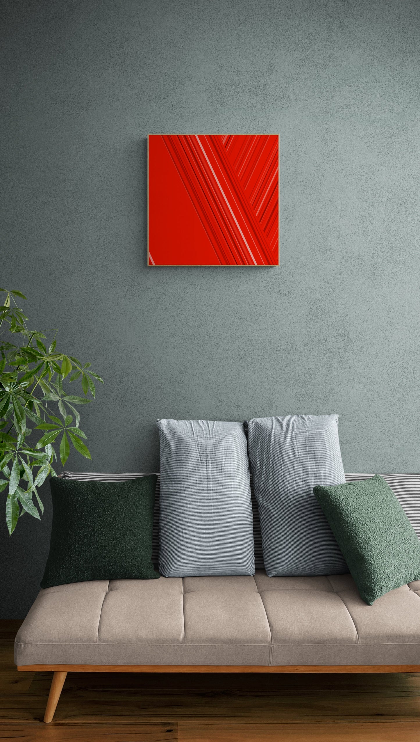 Art print of abstract red design with geometric shapes on a red background on a gray wall above a beige sofa with green and gray cushions.