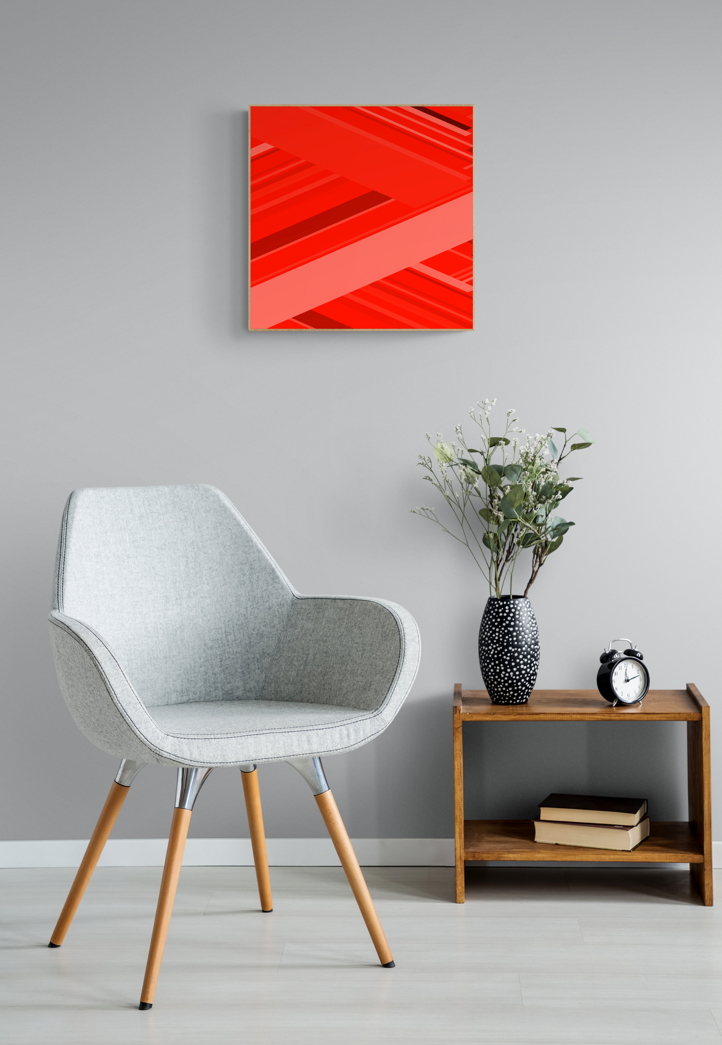 Modern interior with a gray chair, wooden side table, and art print of abstract red design with geometric shapes on a red background