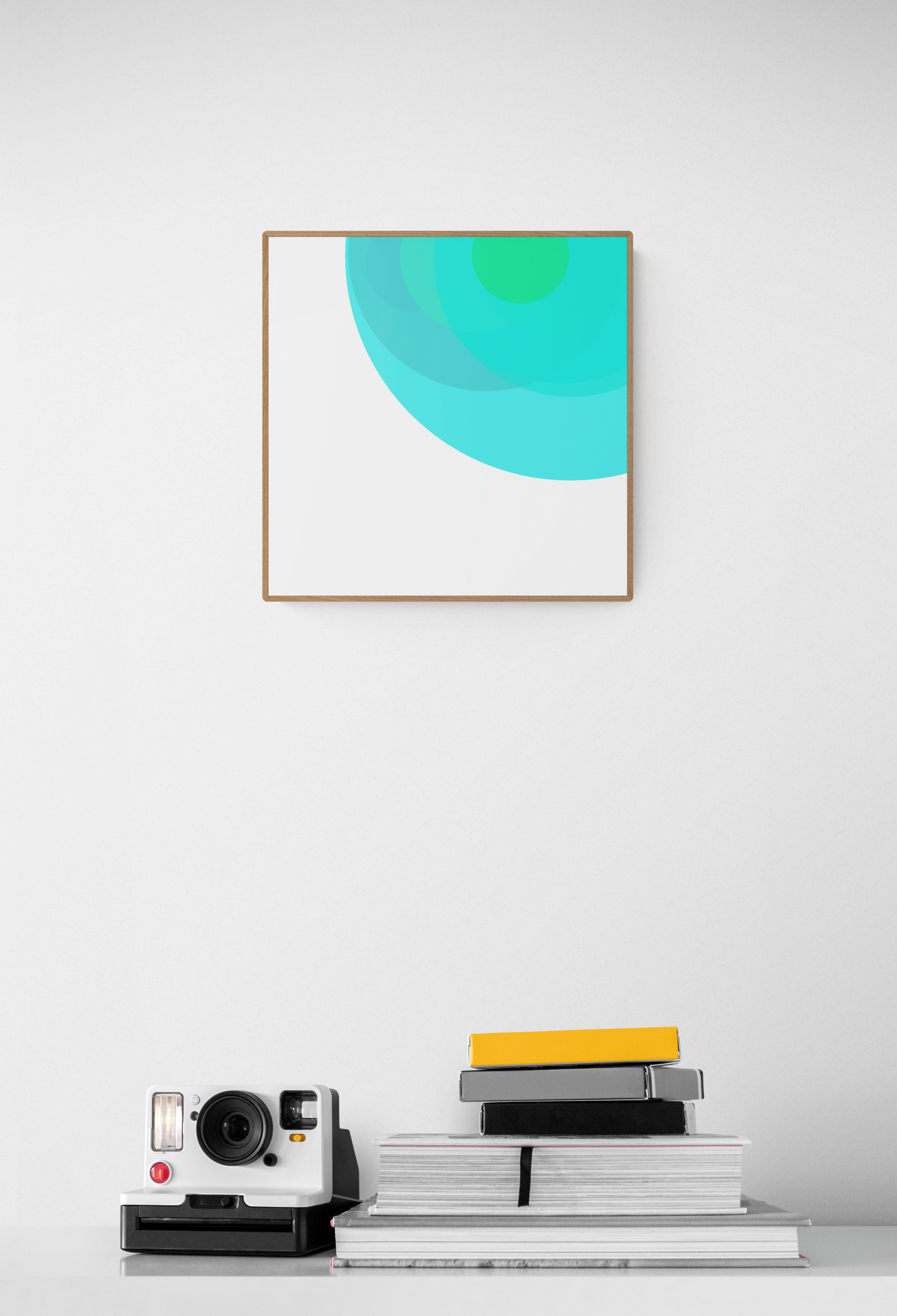 Abstract art print with a gradient of green and blue on a white wall, below which are books and a camera.