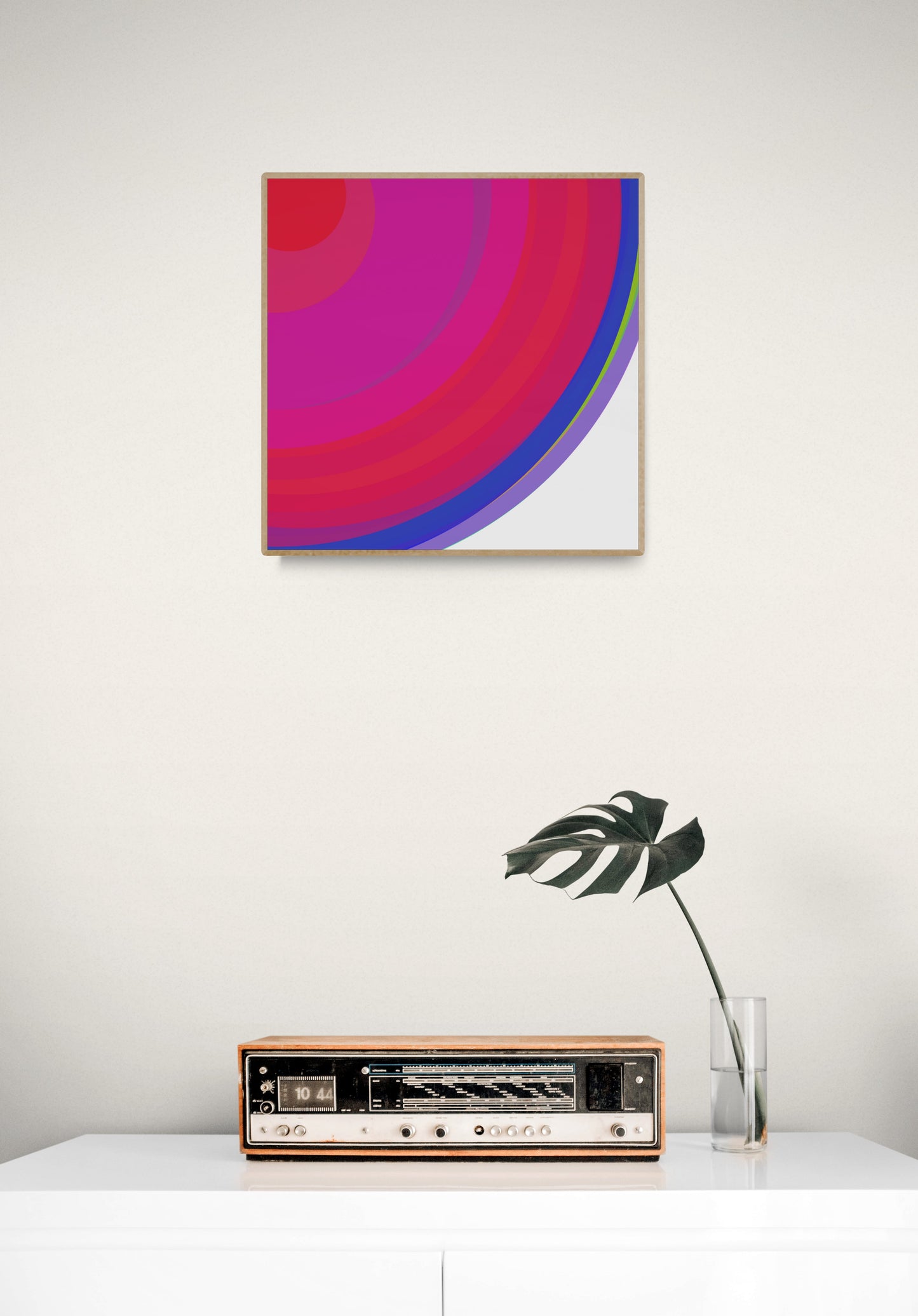Art print of colorful concentric circles with red, pink, and blue on a white background on a white wall above a vintage radio.