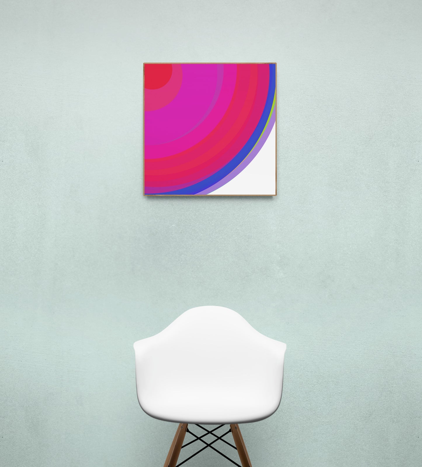 Art print of colorful concentric circles with red, pink, and blue on a white background on a light green wall with a white chair below.