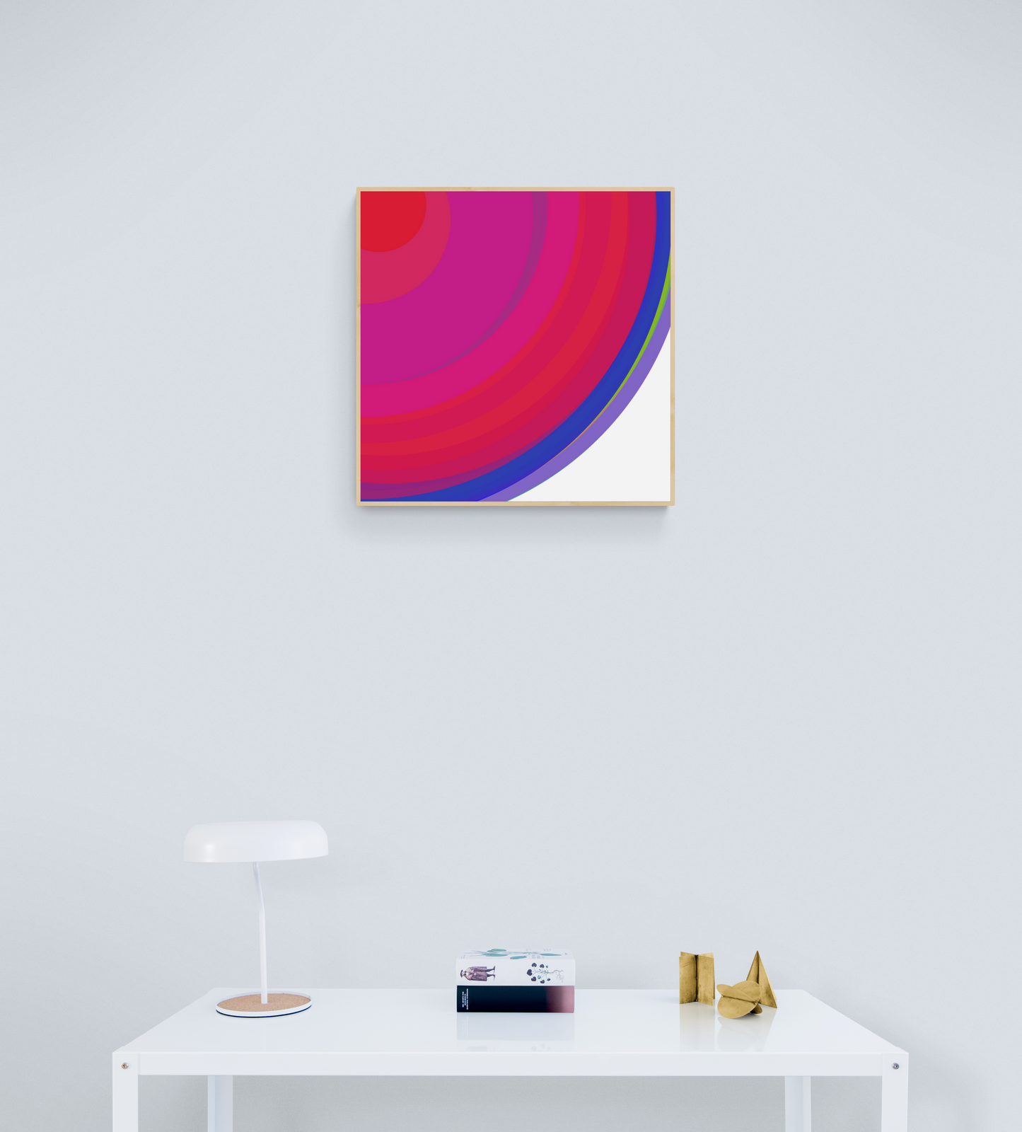 Art print of colorful concentric circles with red, pink, and blue on a white background on a white wall above a white table with decorative items.