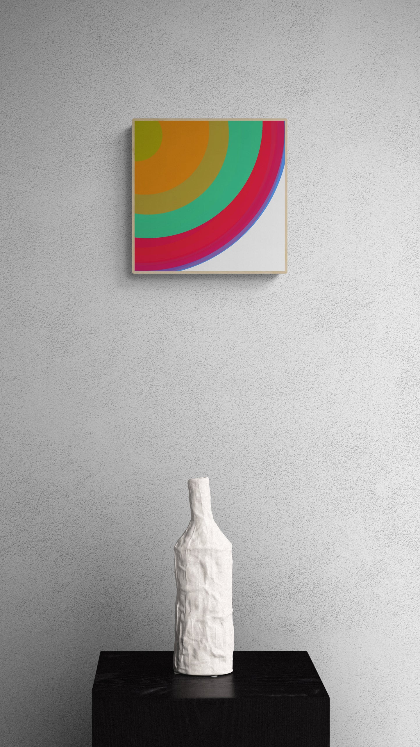 Abstract art print with colorful circular design on a gray wall above a white vase on a black pedestal.