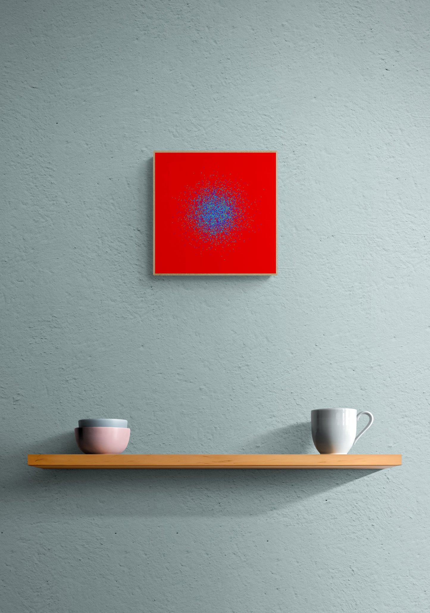 Blue, green, purple confetti like patterned abstract print on a red background on a gray wall above a wooden shelf with two cups.