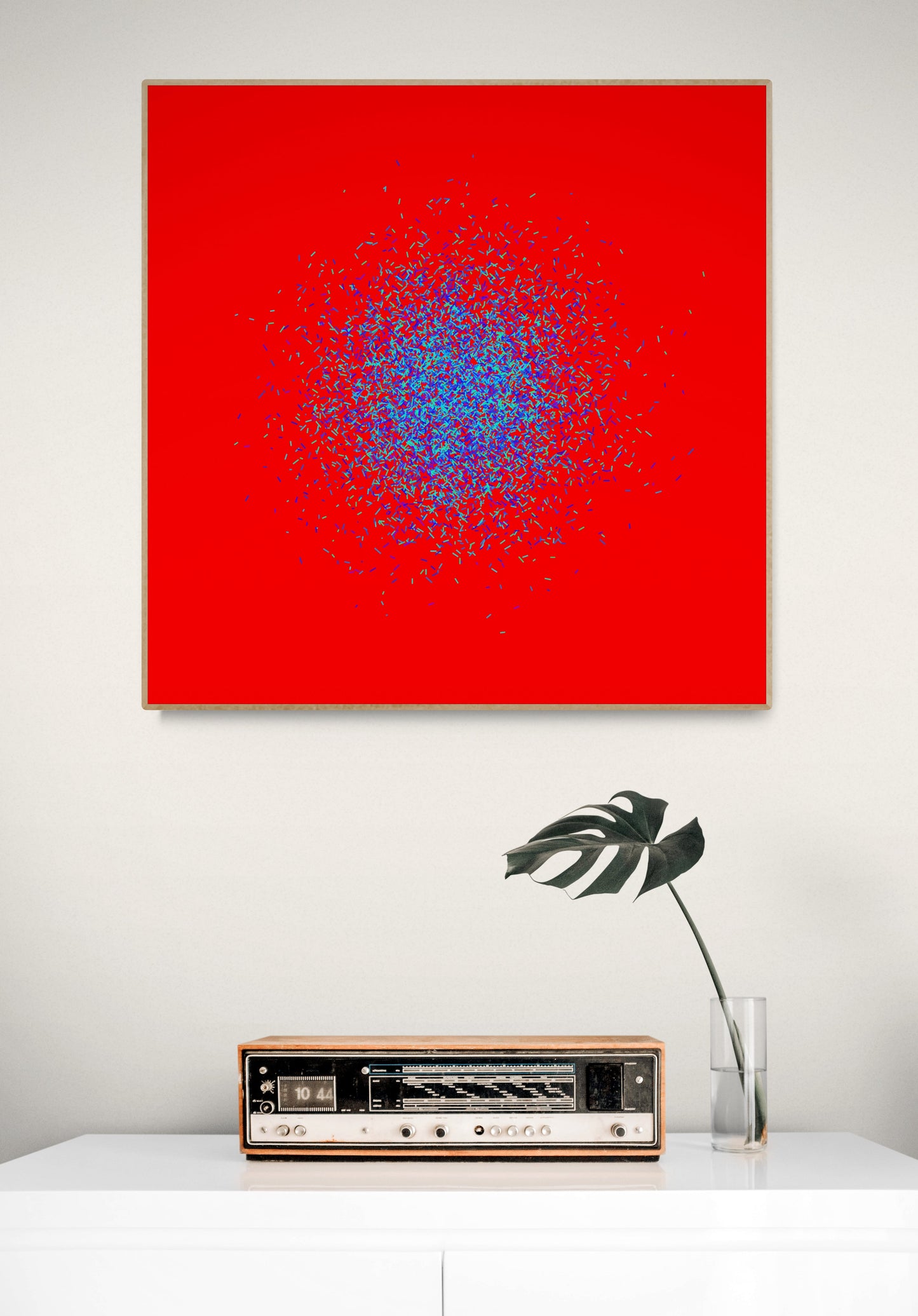 Blue, green, purple confetti like patterned abstract print on a red background, displayed above a table with a vintage radio and plant.
