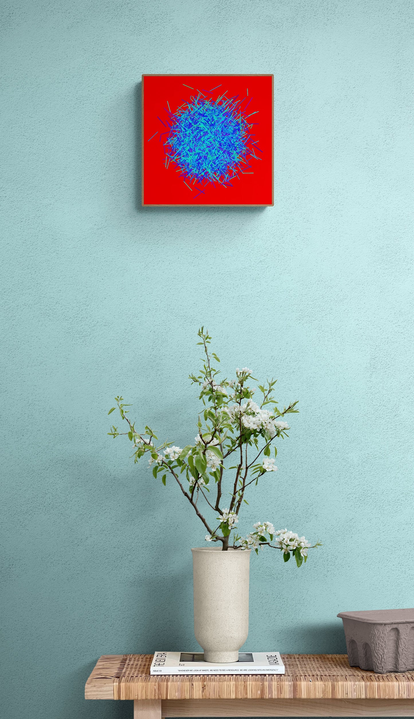Abstract patterned art print of ball of blue and green lines on a red background on a light green wall above a wooden table with a vase and plants.