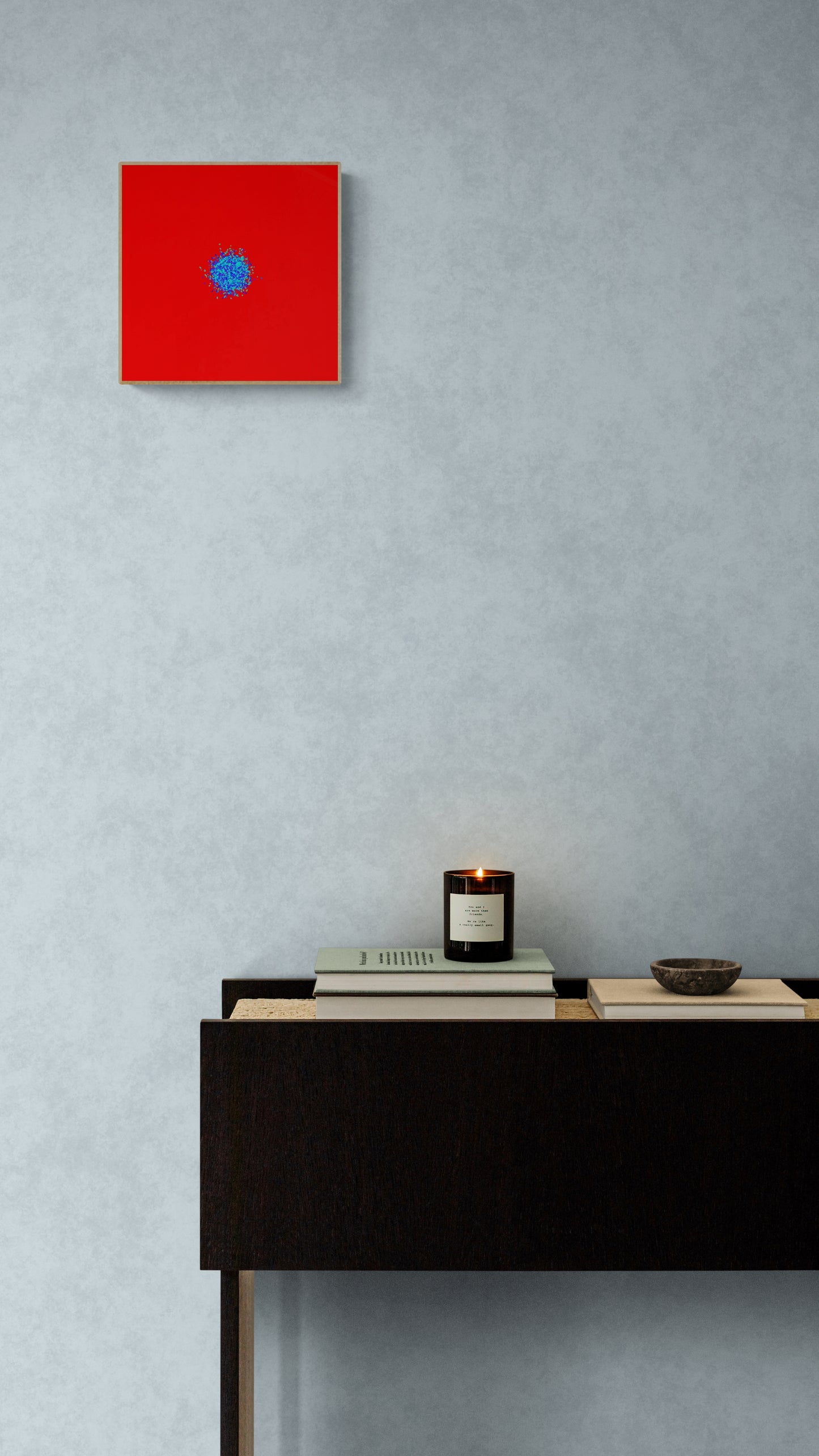 Abstract patterned art print of ball of blue and green fragments on a red background on a gray wall above a black desk.