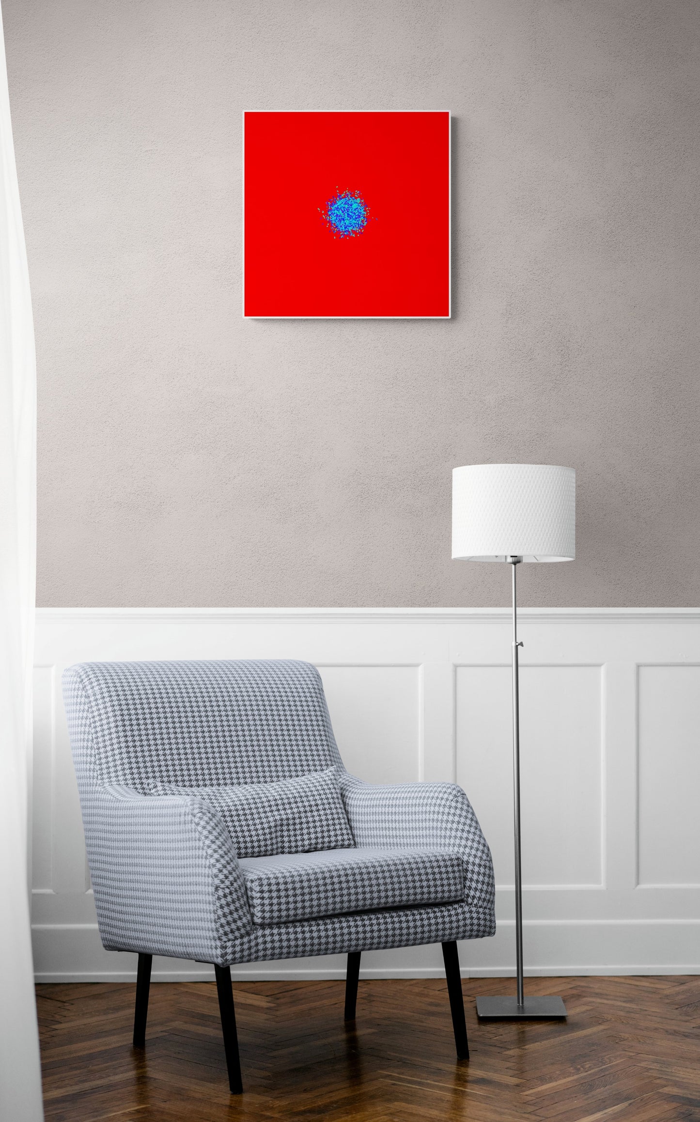 Gray checkered armchair in a room with an abstract patterned art print of ball of blue and green fragments on a red background on the wall.