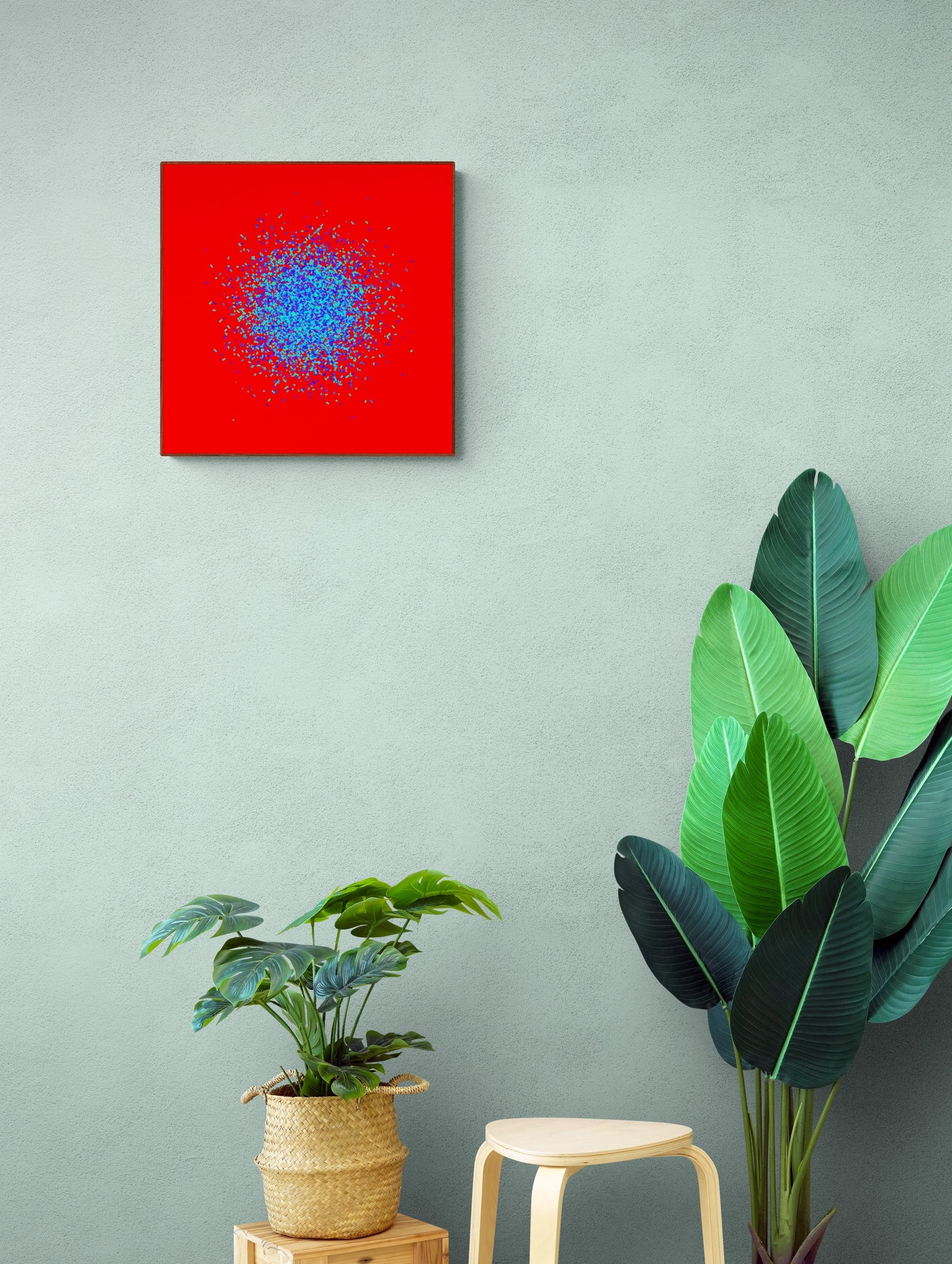 Abstract circle patterned art print of blue and green fragments on a red background, mounted on a light gray wall with plants below.