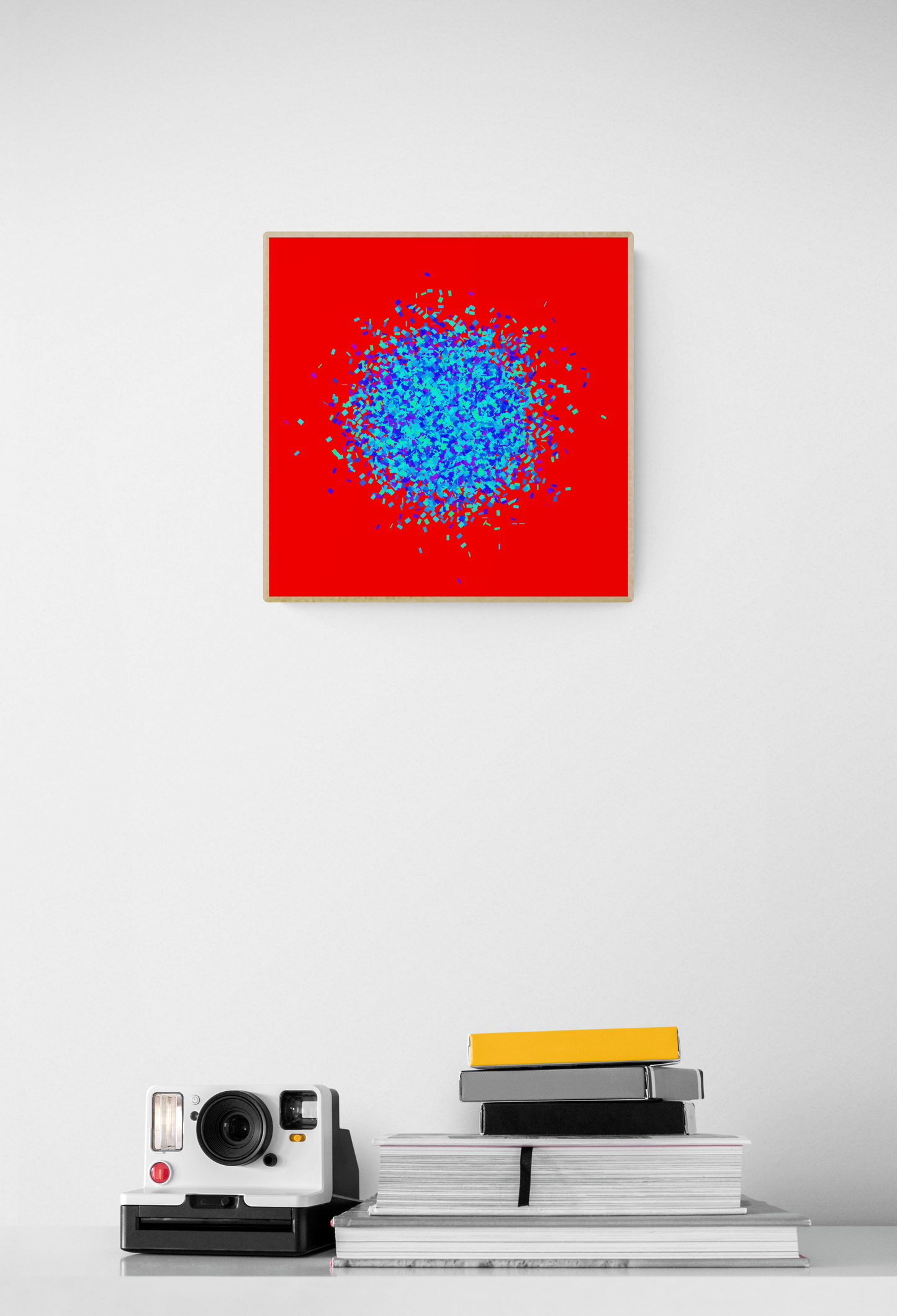 Blue, green, purple confetti like patterned abstract print on a red background on a white wall, below which are books and a camera.