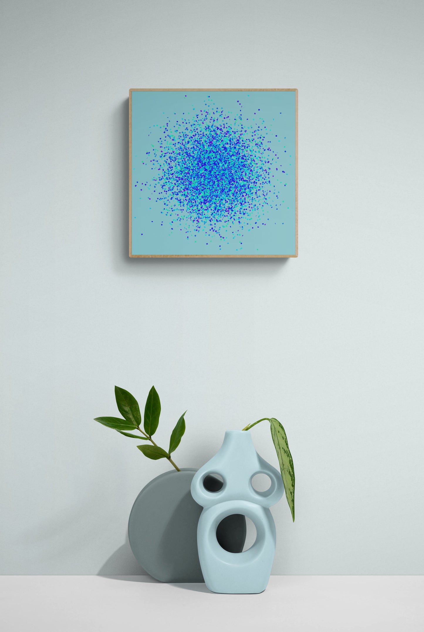 Abstract art print of blue, green and purple confetti like circular pattern on a light blue background on a light gray wall, accompanied by a ceramic sculpture and plant.