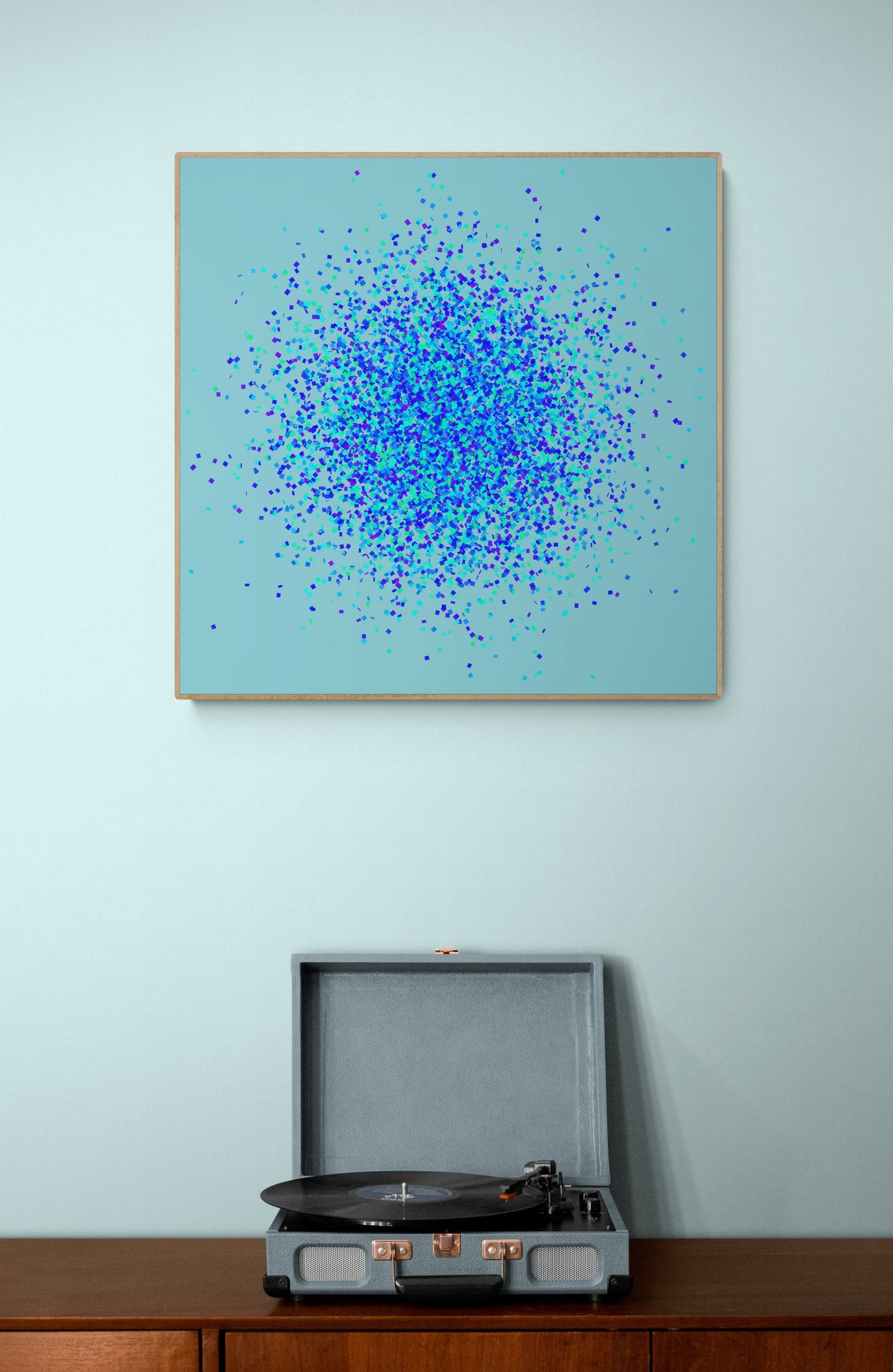 Abstract art print of blue, green and purple confetti like circular pattern on a light blue background on a light blue wall above a record player.
