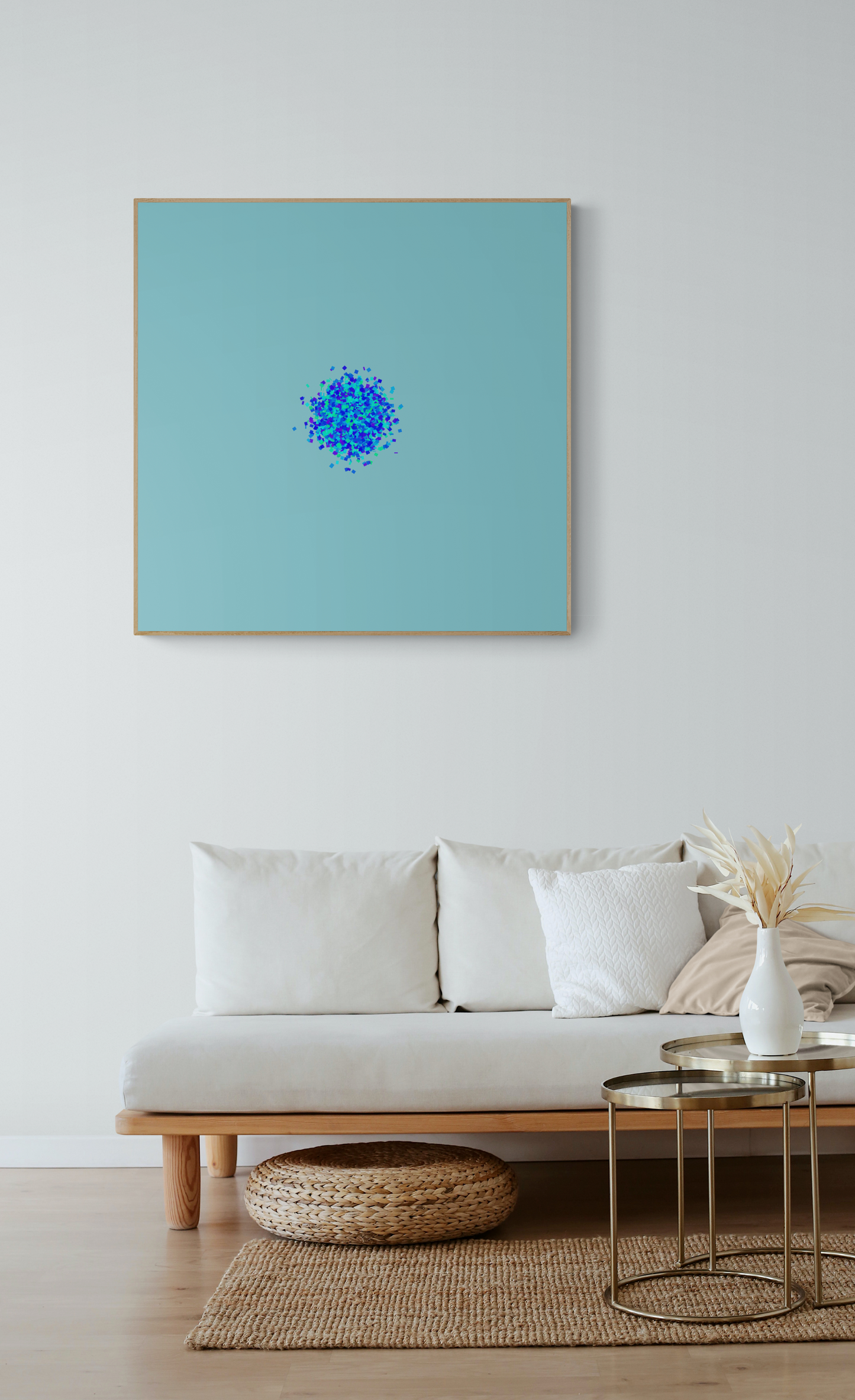 Abstract art print of blue, green and purple confetti like circular pattern on a light blue background on the wall above a white sofa.