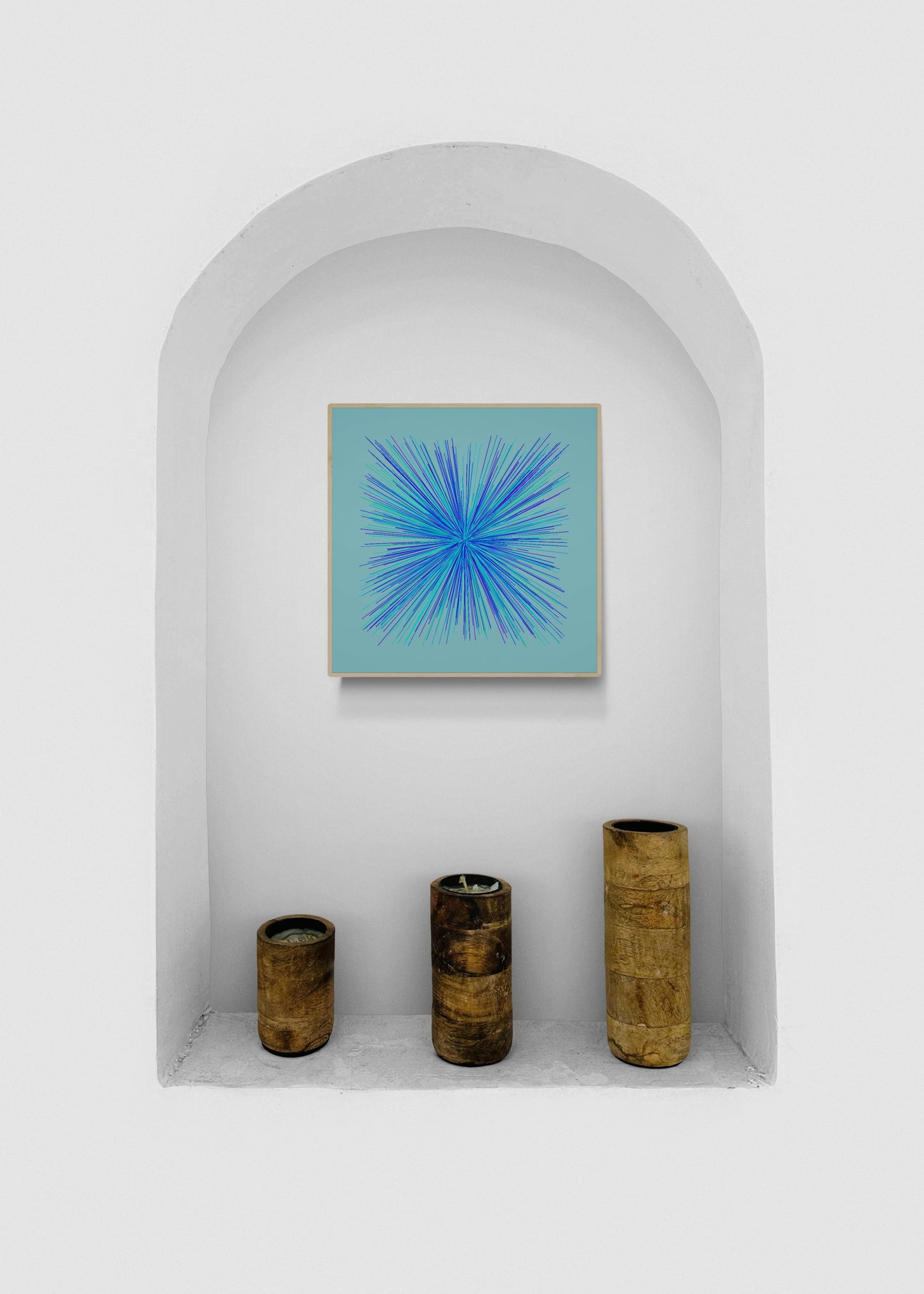 Decorative setup with an abstract art print of blue, green and purple lines in a radial burst pattern on a light blue background and three cylindrical bamboo vases in a white alcove.