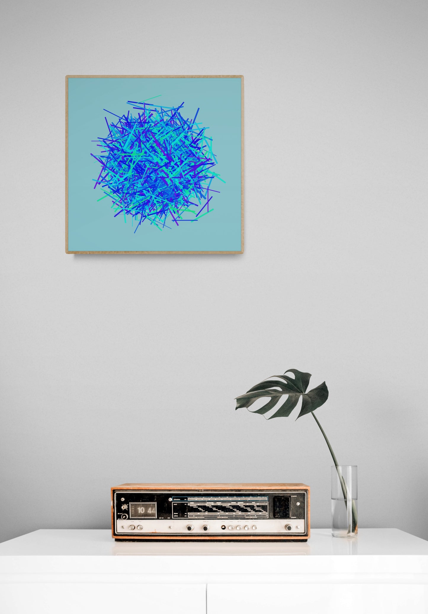 Abstract art print of blue, green and purple lines in a circular pattern on a light blue backgroundon a light gray wall above a vintage radio.