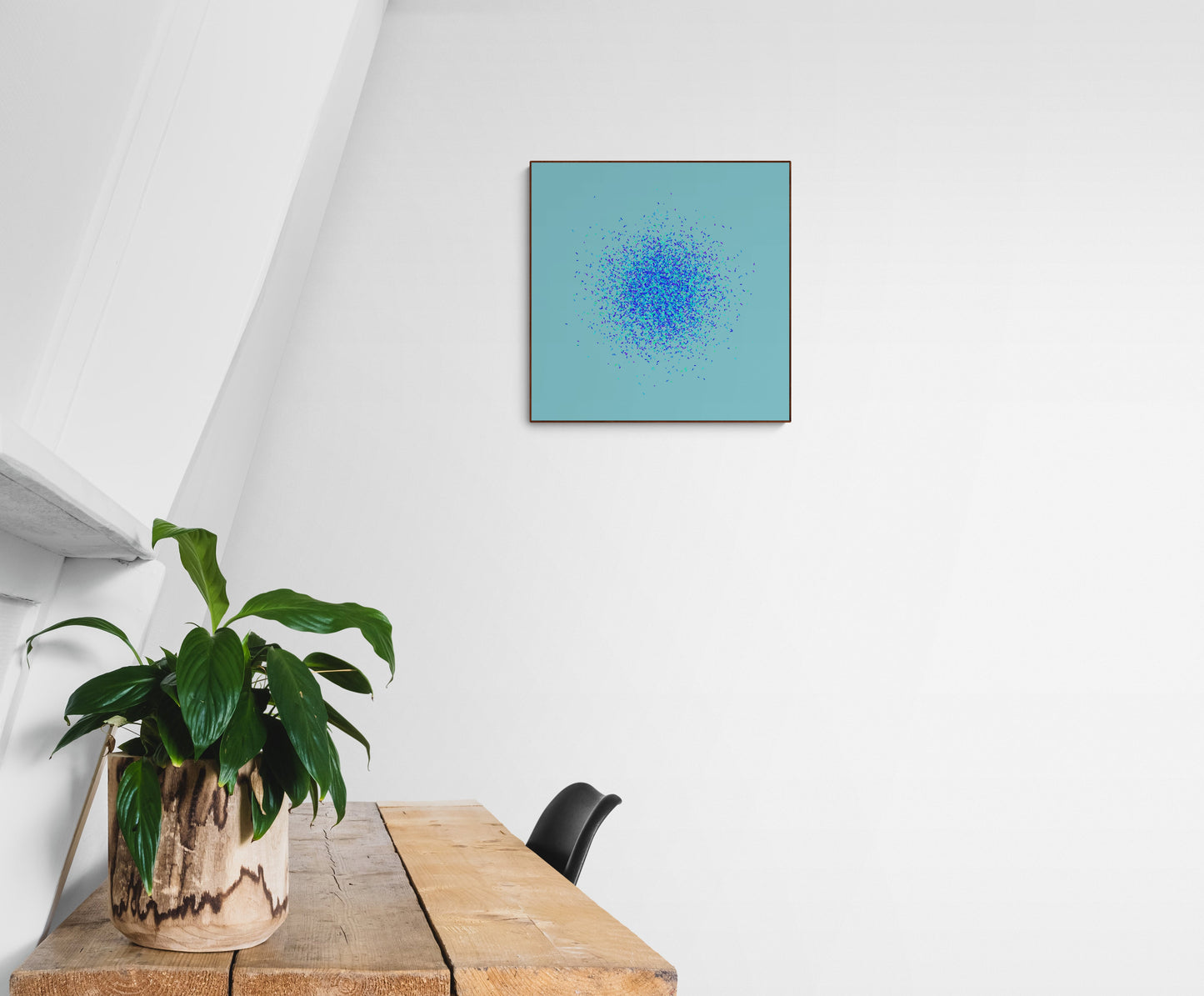 Abstract art print of blue, green and purple confetti like circular pattern on a light blue background on a white wall above a wooden table with a plant.
