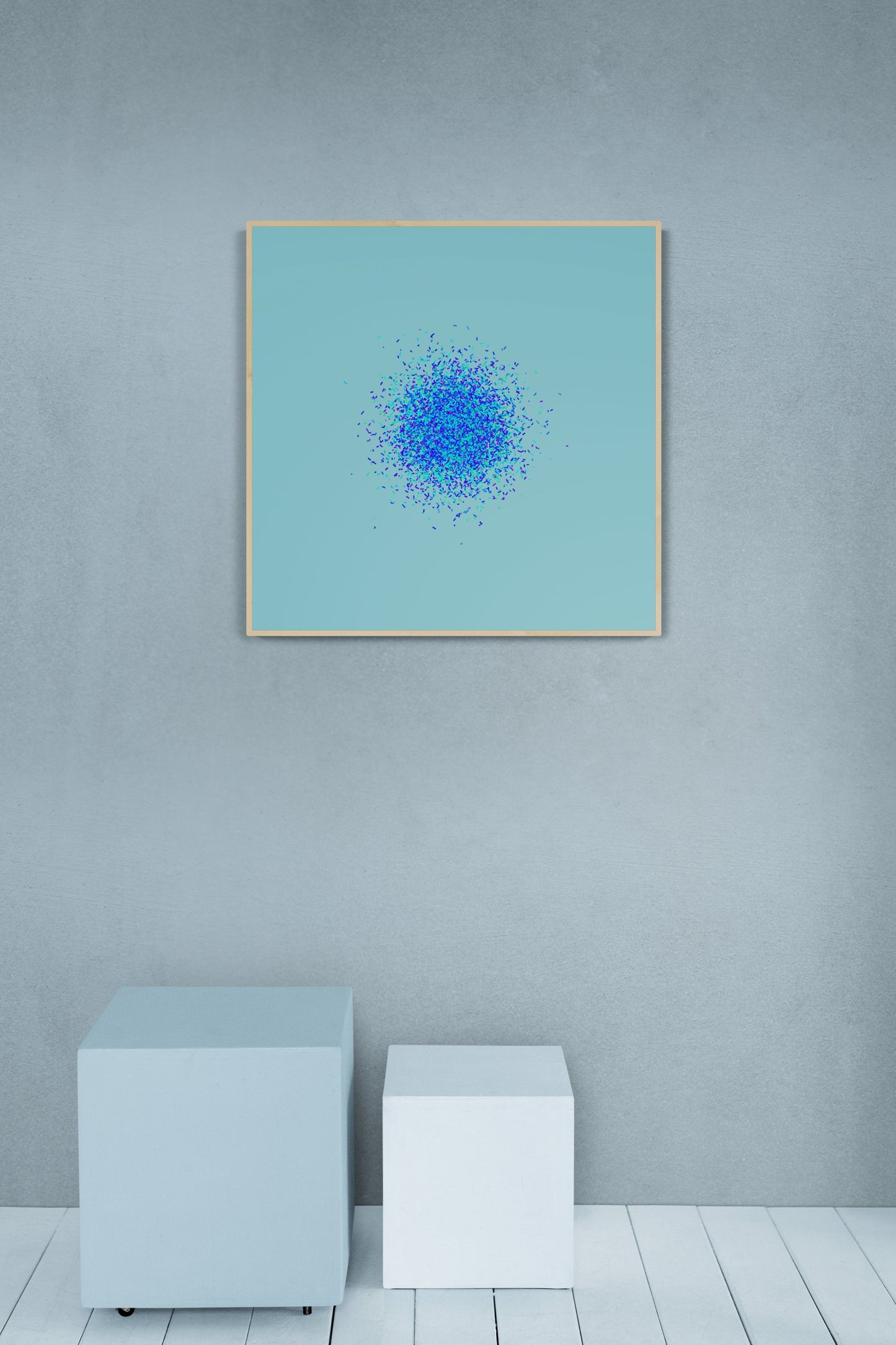 Framed abstract art print of blue, green and purple confetti like circular pattern on a light blue background on a light gray wall.