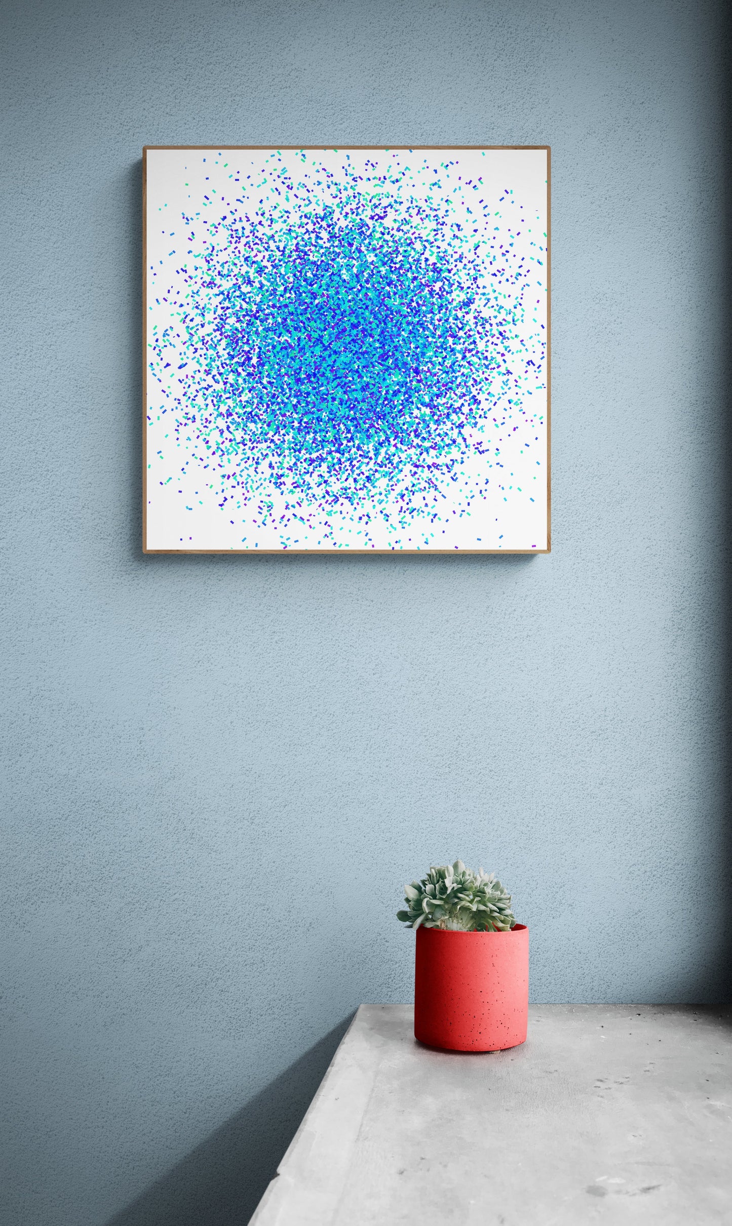 Blue, green and purple confetti like patterned abstract art print on a white background on a gray wall, accompanied by a red pot with a plant.