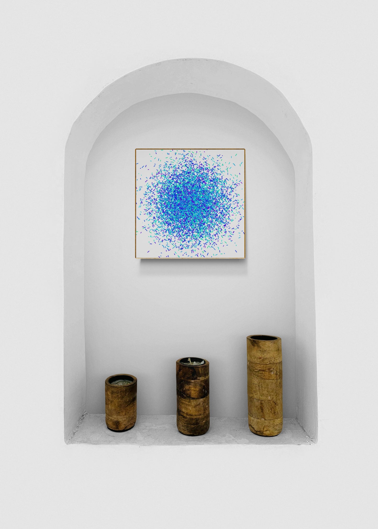 Colorful green blue confetti patterned abstract art print on a white background and three cylindrical objects in a white alcove.
