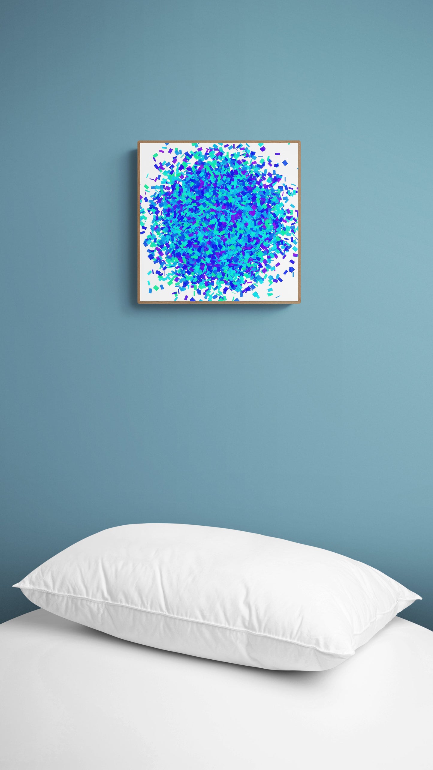 Colorful green blue confetti like patterned abstract art print on a white background on a wall above a bed with white pillows.
