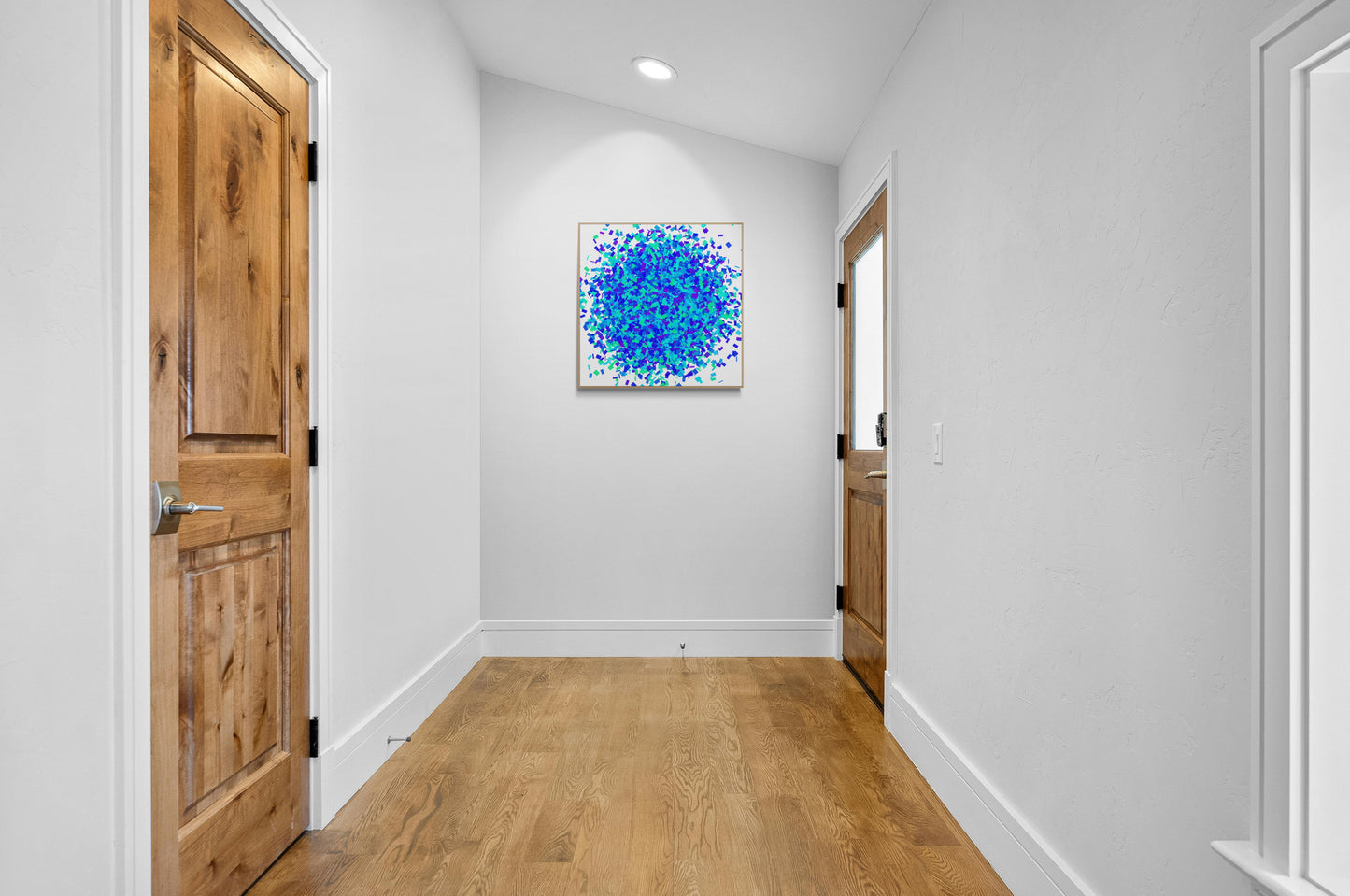 Foyer with wooden doors and colorful green blue confetti like patterned abstract art print on a white background on the wall.