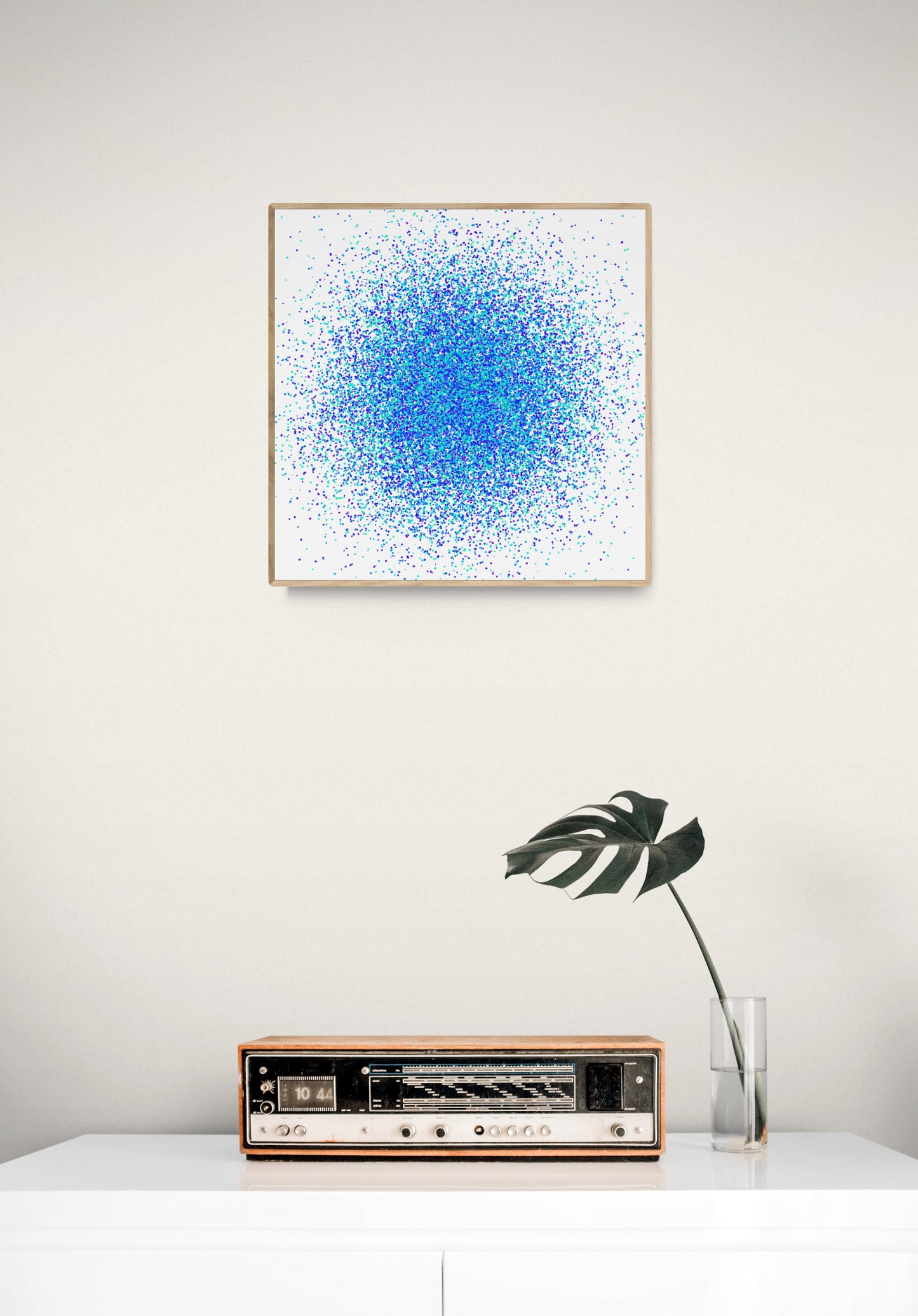 Colorful abstract blue and green dot like patterned art print above a vintage radio on a white surface.