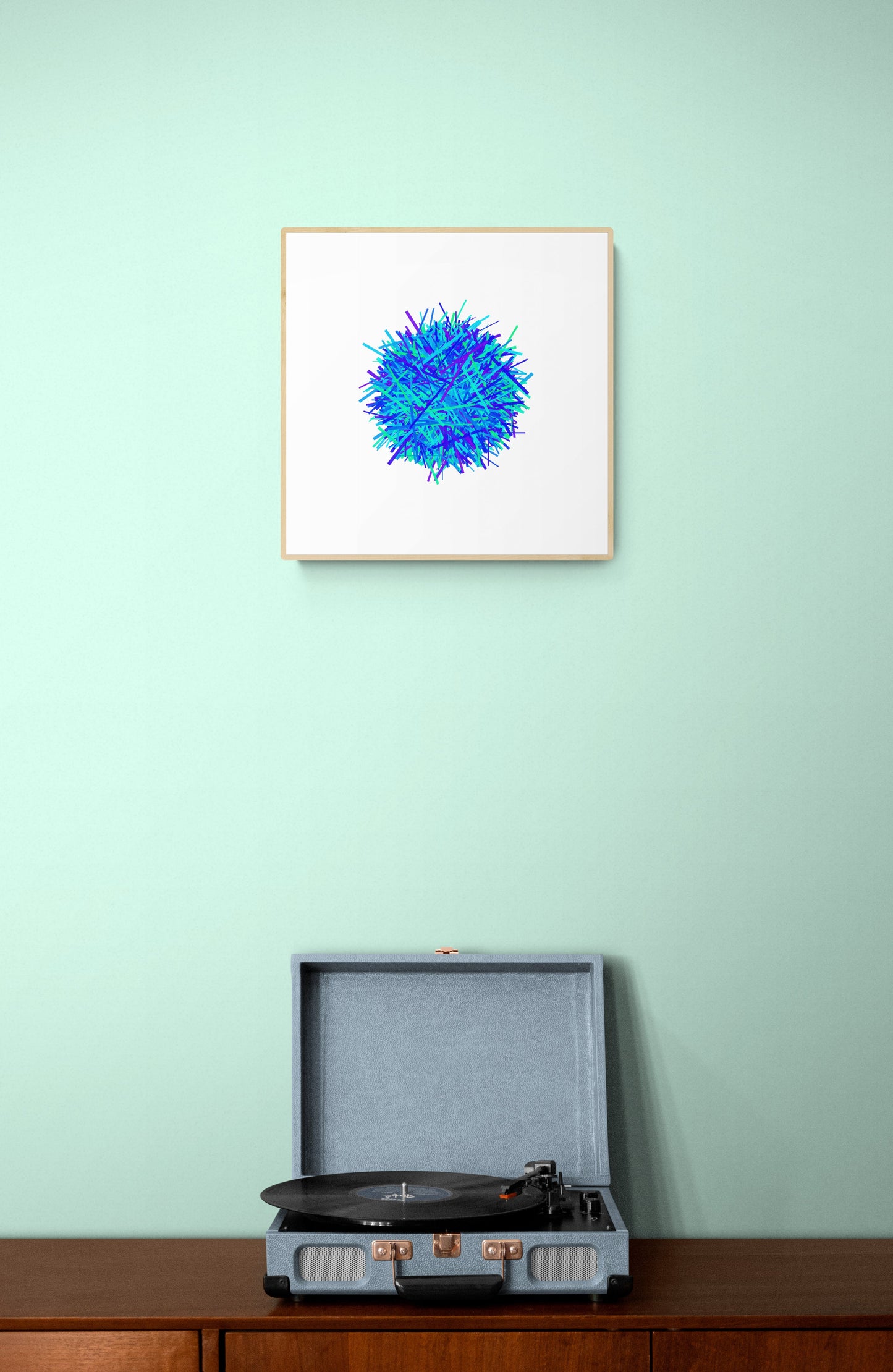 Framed blue abstract artwork print on a light green wall above a record player.