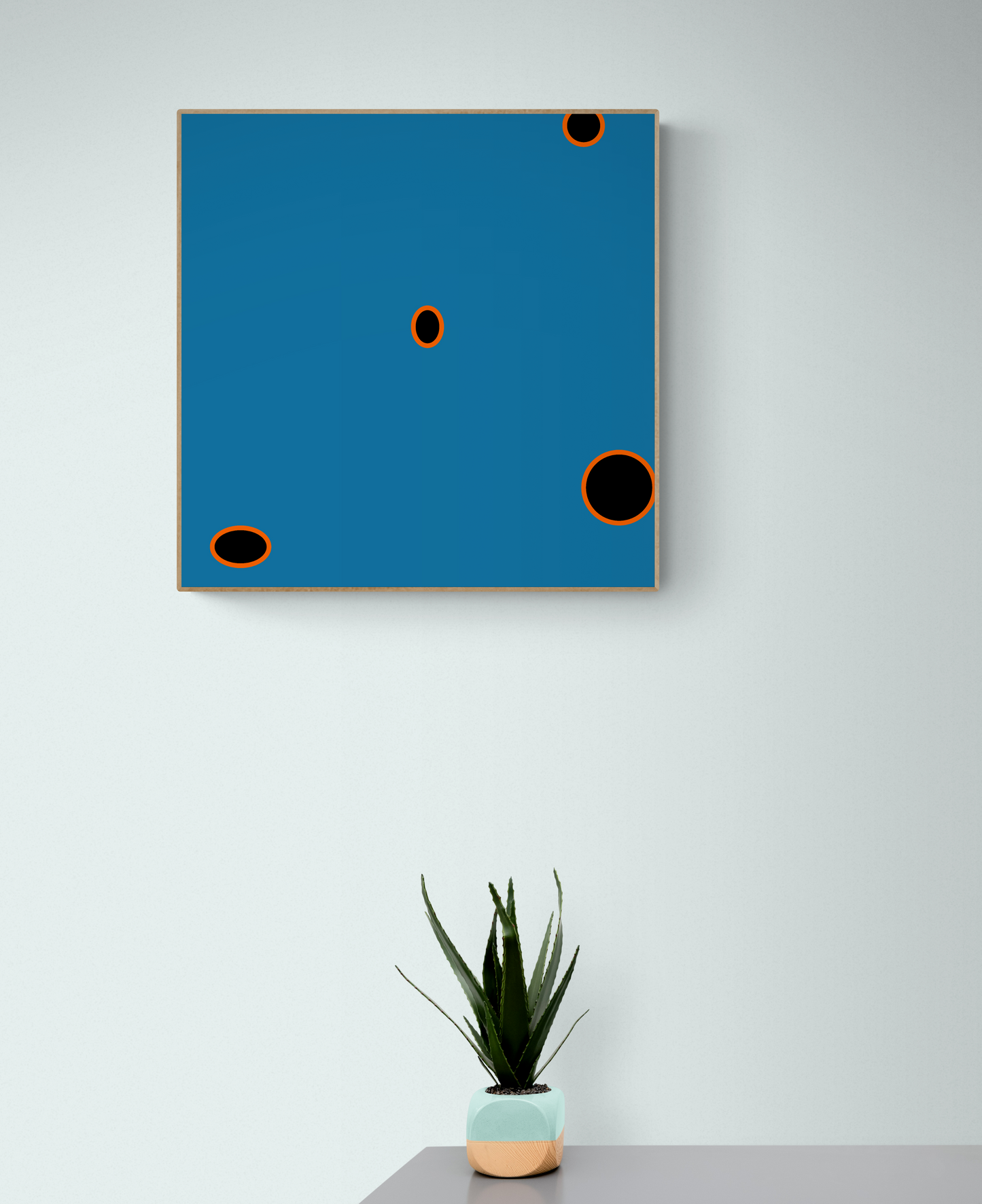 Abstract art print with blue background and black circles on a white wall, with a potted plant below.
