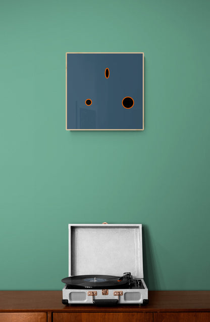 Record player on a wooden surface with a framed grey abstract art print on a green wall.