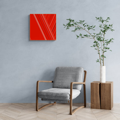 Modern interior with a gray armchair, art print of abstract red design with geometric shapes on a red background, and a plant on a wooden side table.
