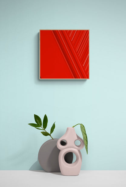 Art print of abstract red design with geometric shapes on a red background on a light blue wall with two decorative vases and a plant.