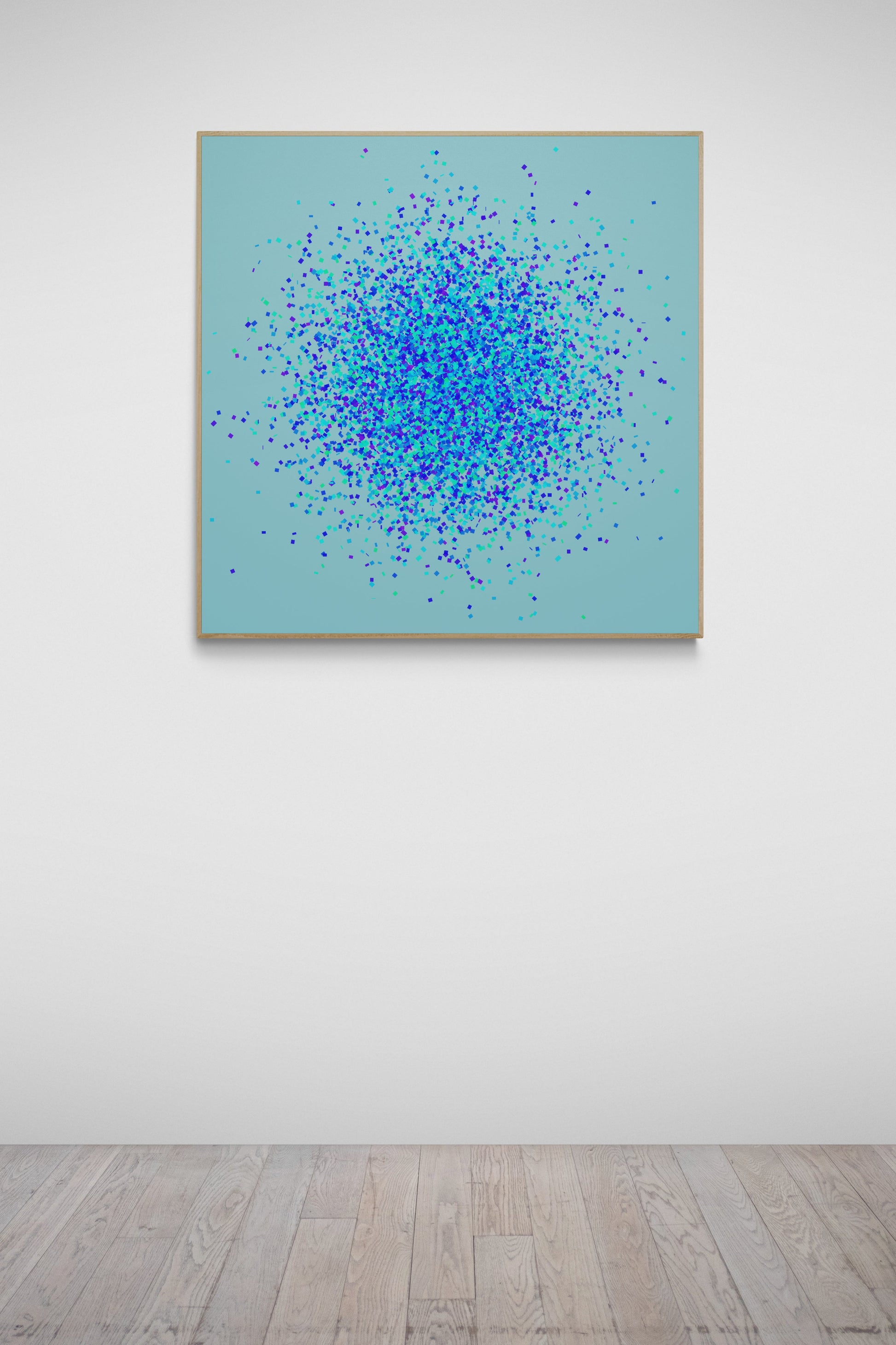 Abstract art print of blue, green and purple confetti like circular pattern on a light blue background, framed in gold, hanging on a white wall.