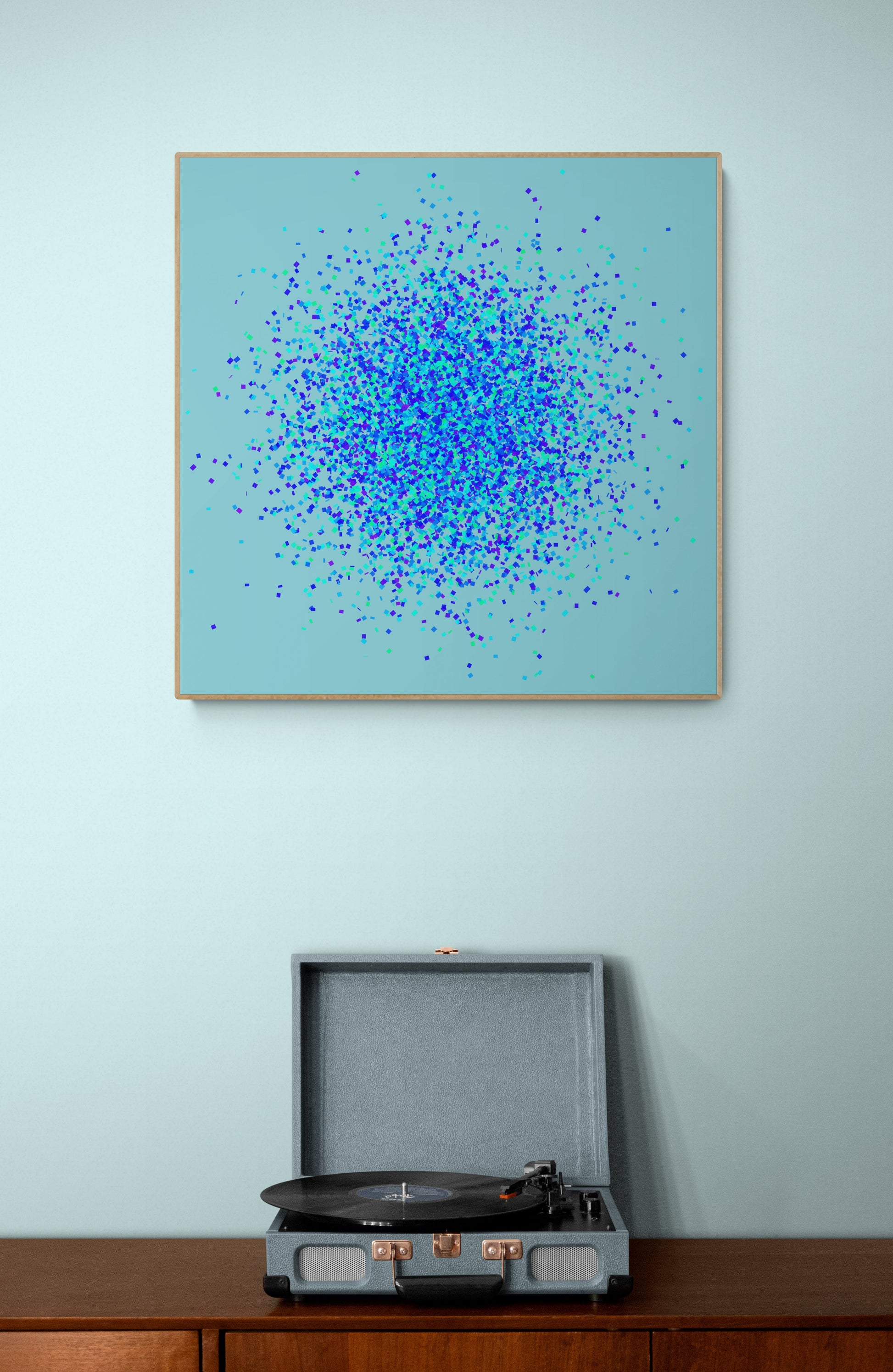 Abstract art print of blue, green and purple confetti like circular pattern on a light blue background on a light blue wall above a record player.