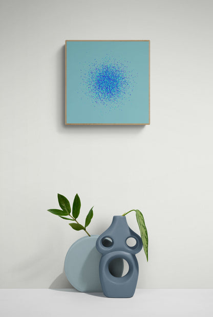 Framed abstract art print of blue, green and purple confetti like circular pattern on a light blue background on a white wall, accompanied by two ceramic vases.