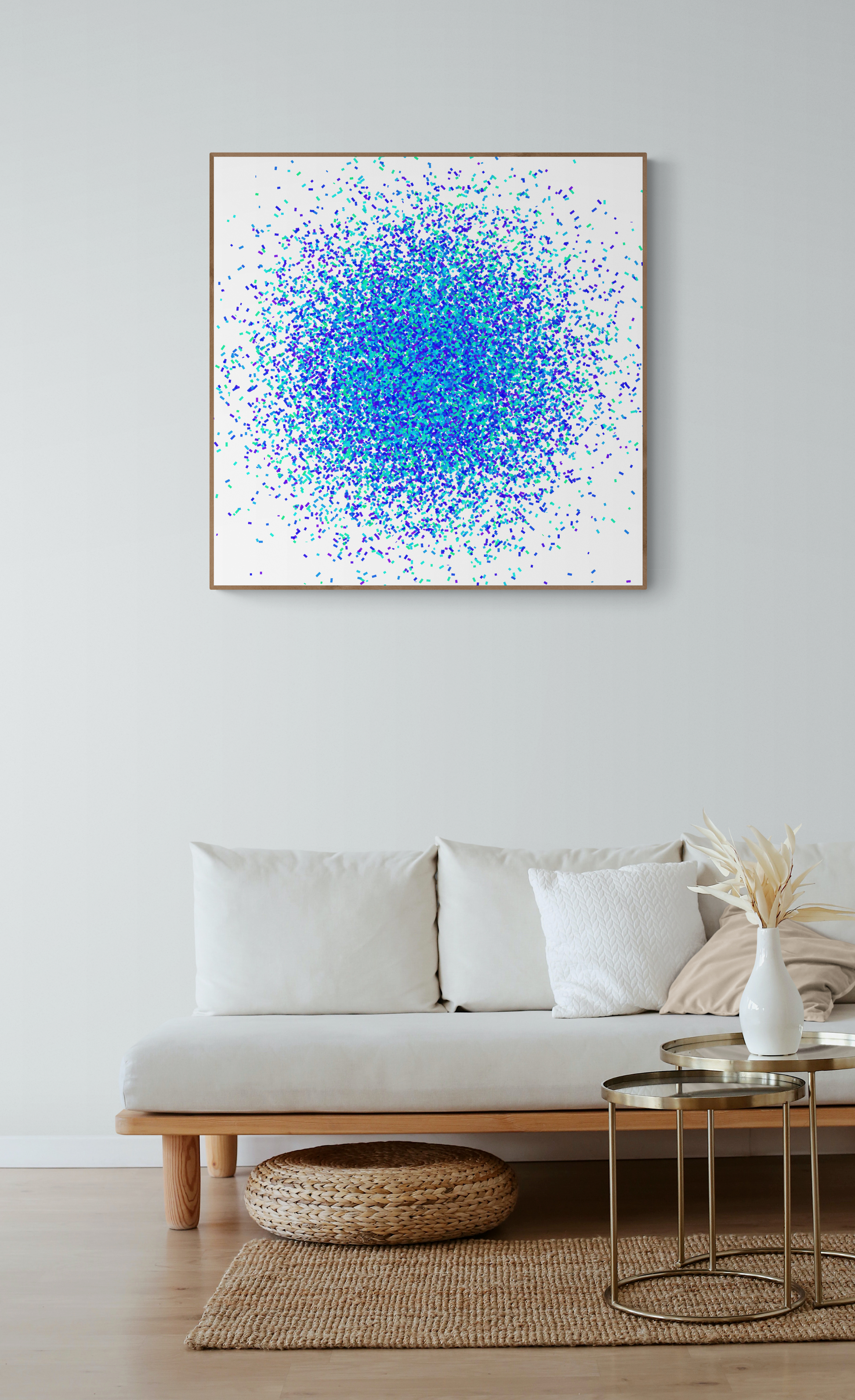 Blue, green and purple confetti like patterned abstract art print on a white background on a wall above a white sofa in a living room.