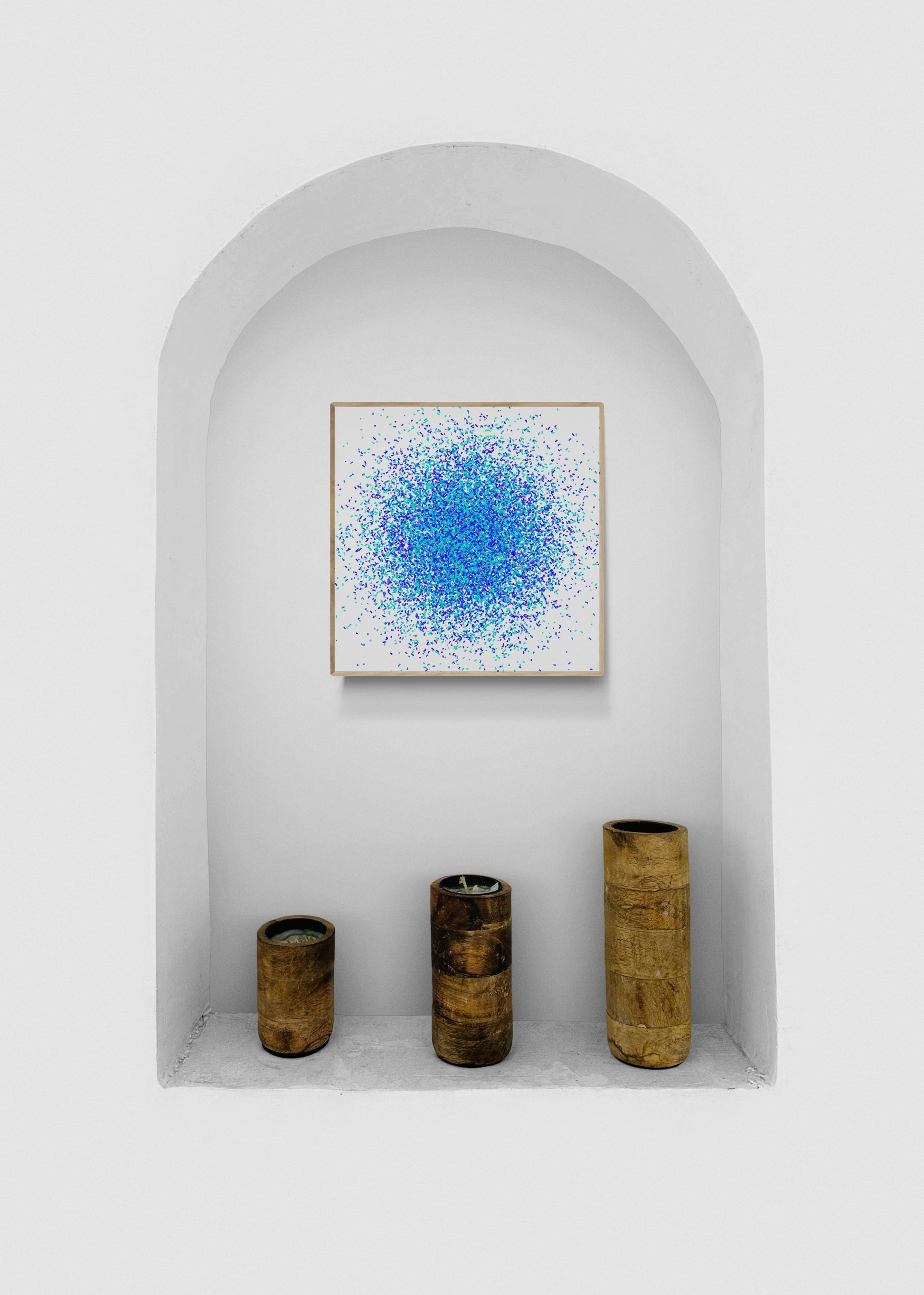 Blue, green and purple confetti like patterned abstract art print on a white background and three cylindrical objects in a white alcove.