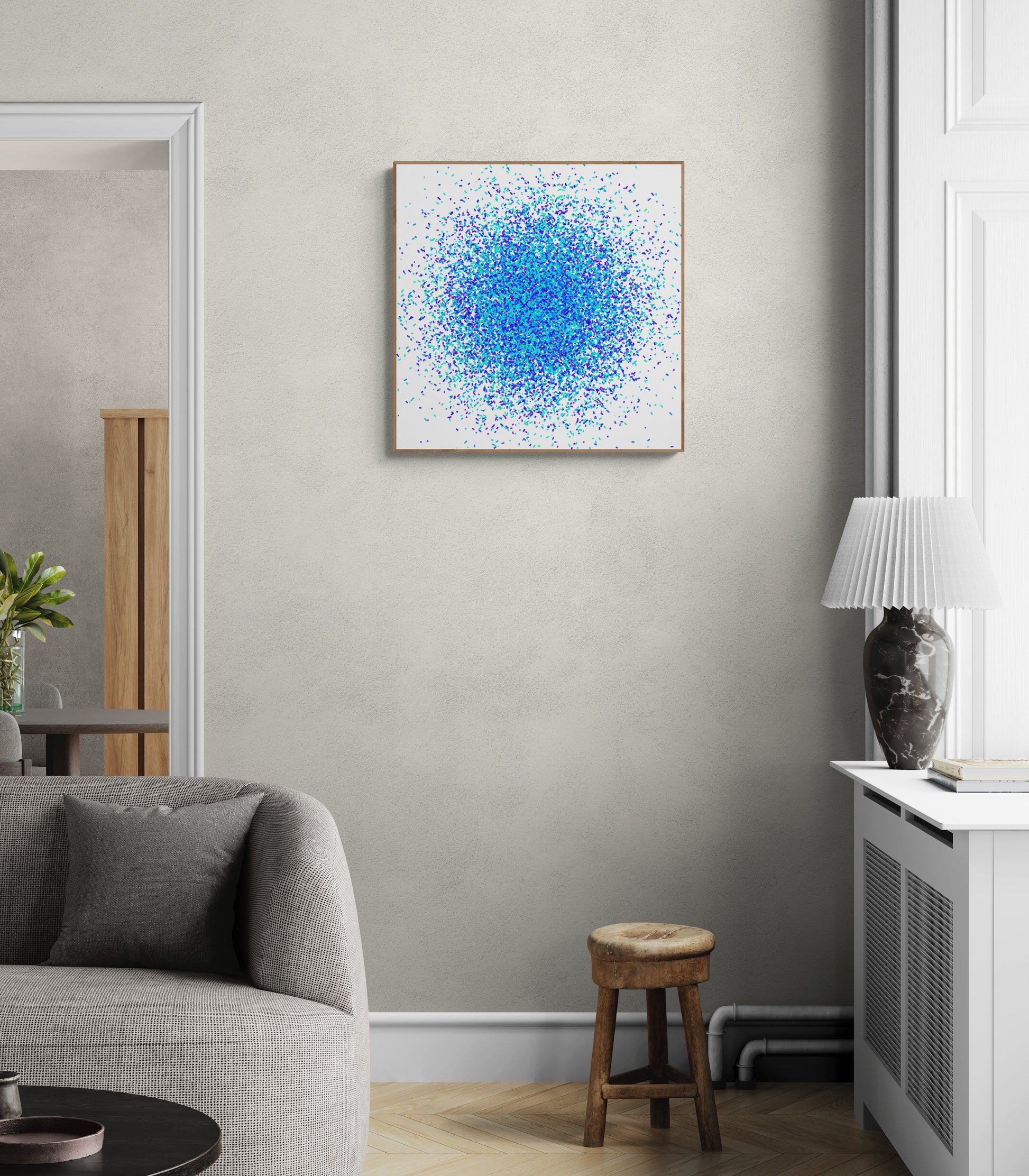 Blue, green and purple confetti like patterned abstract art print on a white background on a gray wall above a sofa in a living room.