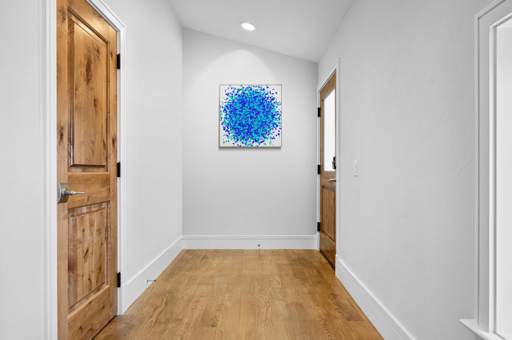 Foyer with wooden doors and colorful green blue confetti like patterned abstract art print on a white background on the wall.
